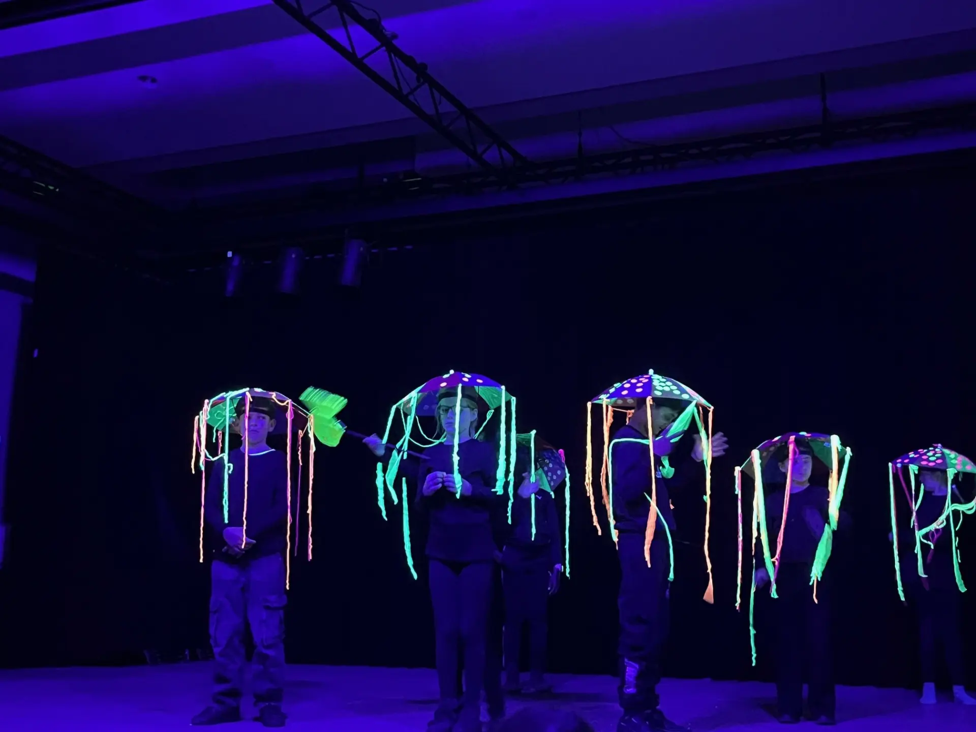 Mit Schwarzlichtfarben bemalte Schüler*innen treten auf einer Bühne auf