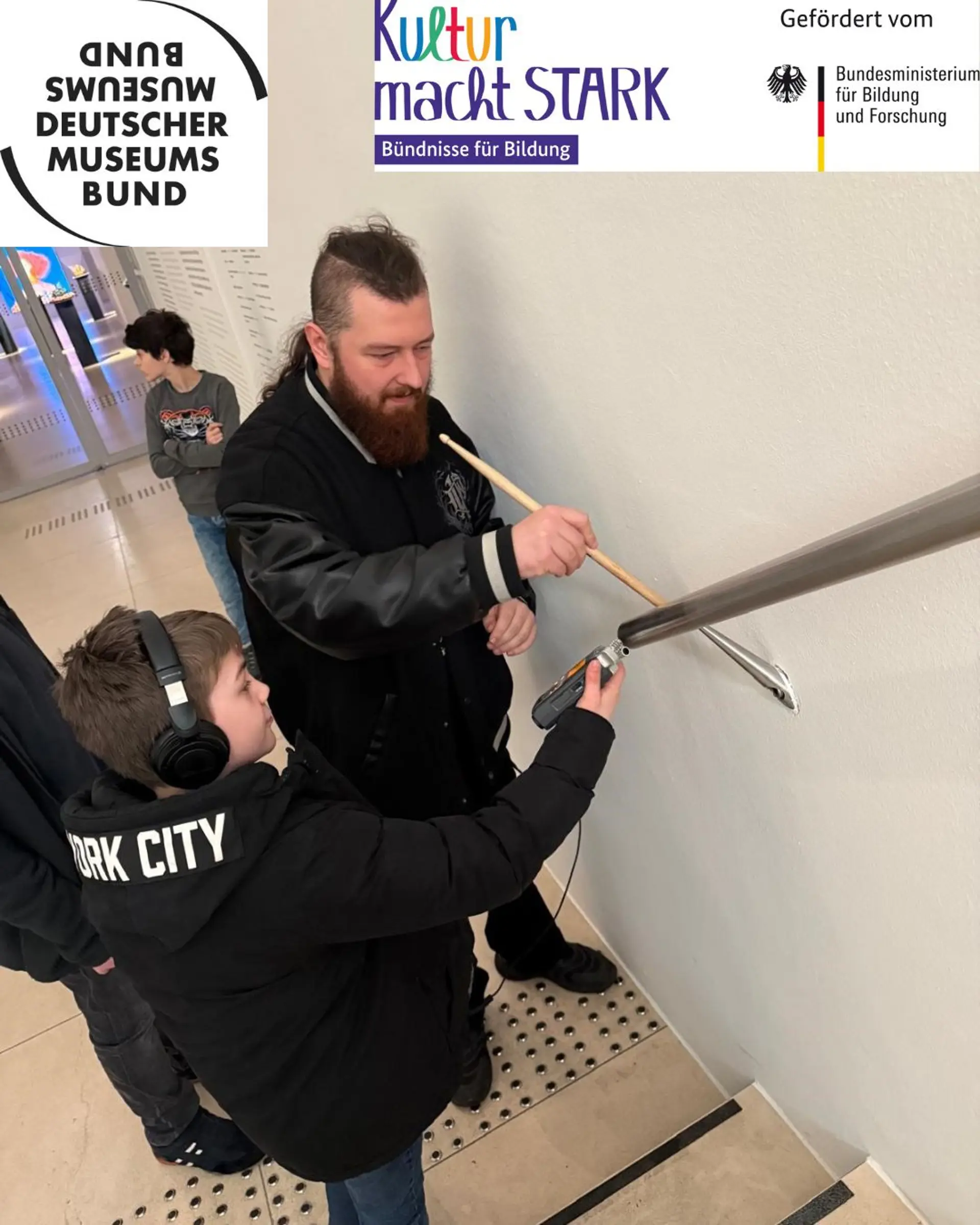 Ein Mann und ein Kind halten ein Mikrofon an ein Treppengeländer