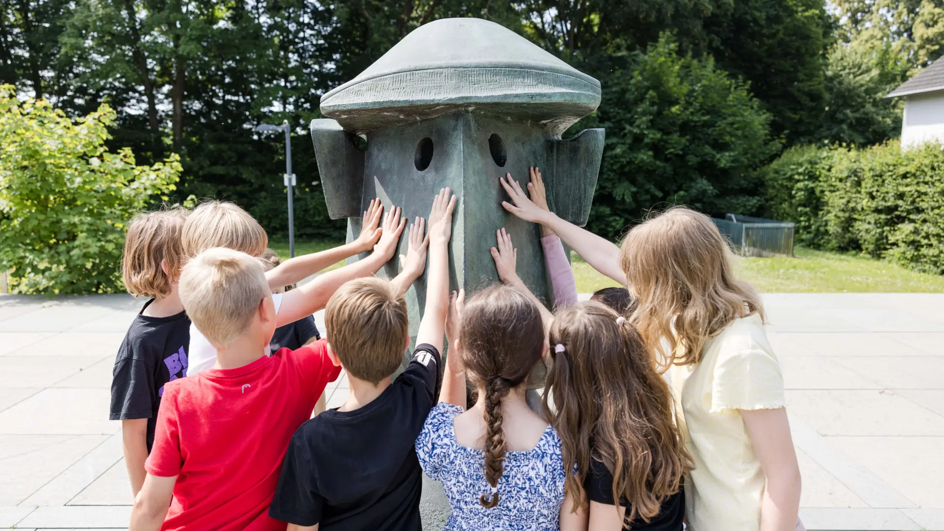 Eine Gruppe von Kindern fasst zusammen eine große Skulptur im Außenbereich des Museums an