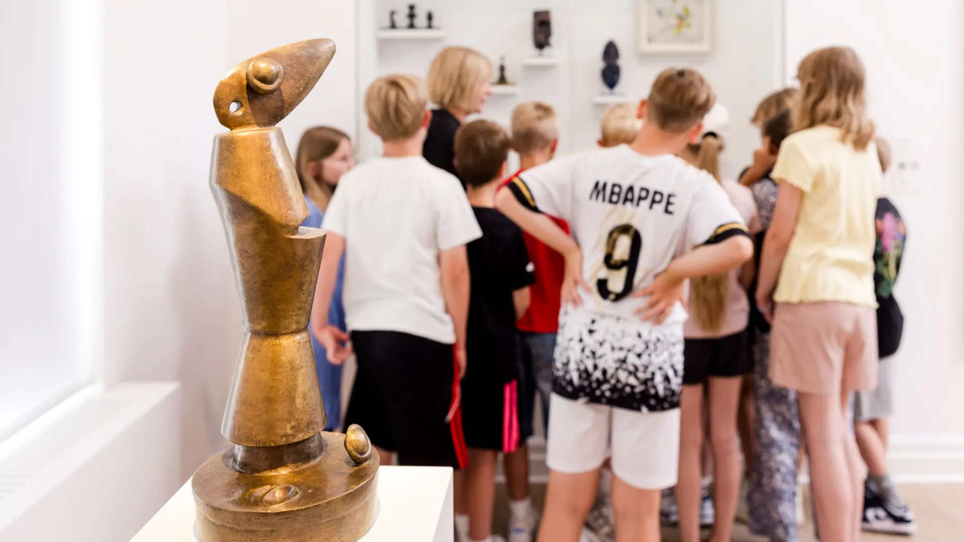 Gruppe Kinder steht vor einer Vitrine, davor eine Skulptur