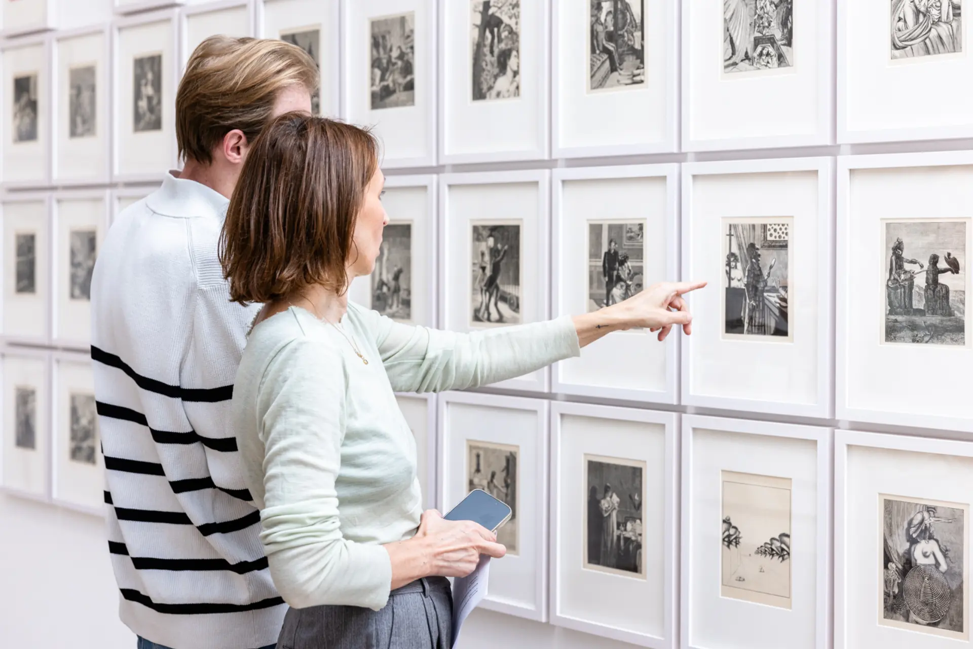 Zwei Personen vor Grafikserie, eine zeigt auf ein Werk