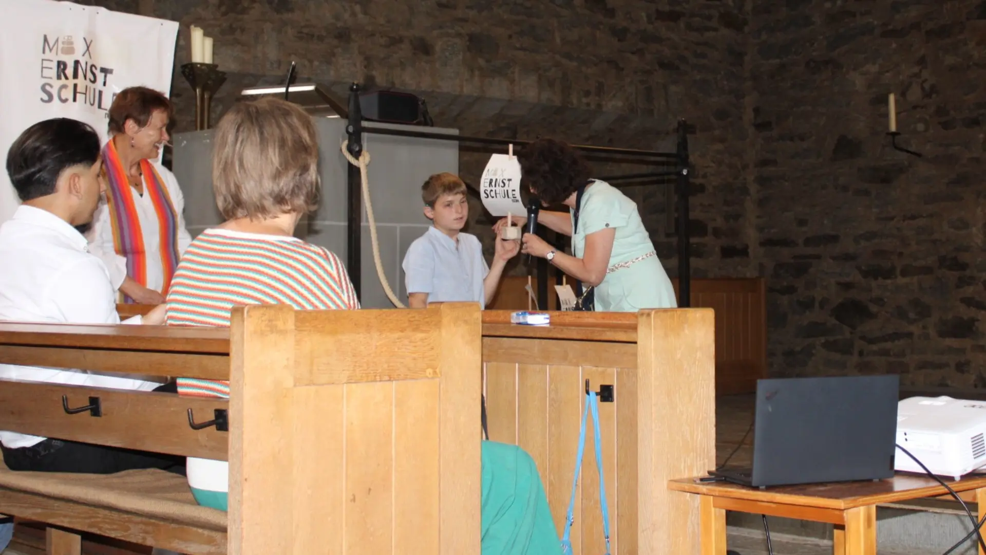 Innenraum der Kirche. Schüler und Lehrer stehen vor Segelschiff. Schüler hält ein kleines Schiff in der Hand