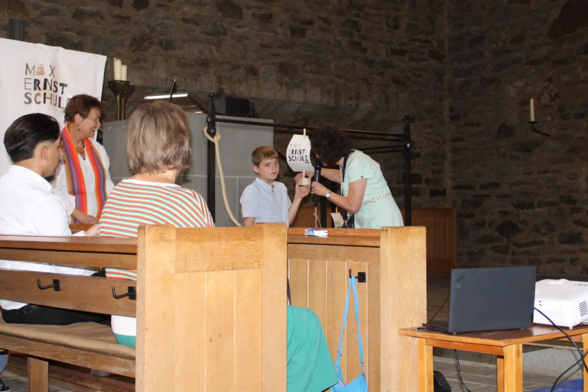 Innenraum der Kirche. Schüler und Lehrer stehen vor Segelschiff. Schüler hält ein kleines Schiff in der Hand
