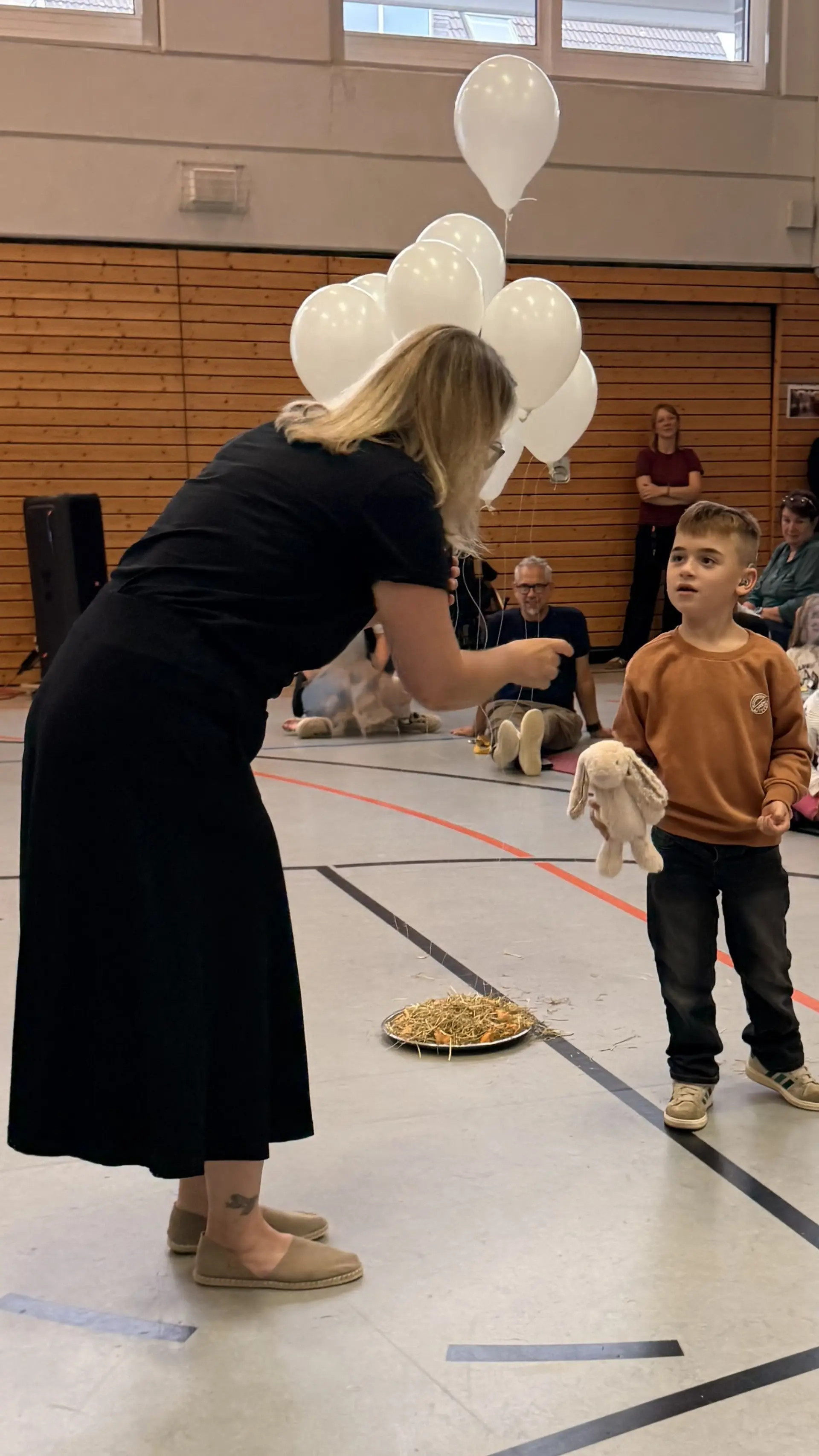 Junge kommt mit Hasenkuscheltier nach vorne zu seiner Lehrerin