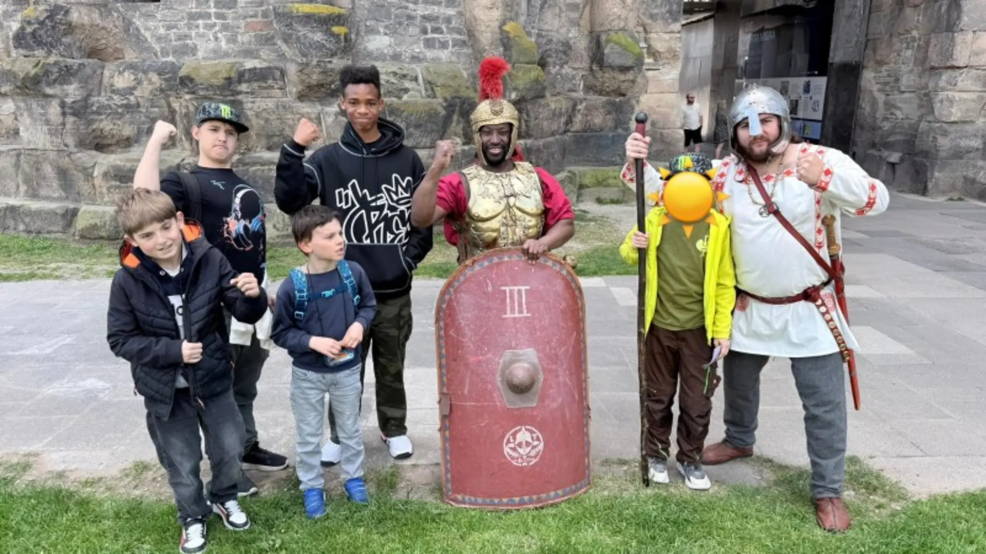 Gruppenbild vor der Porta Nigra: fünf Kinder stehen neben zwei Erwachsenen, die als römischer Gladiator und germanischer Krieger verkleidet sind.