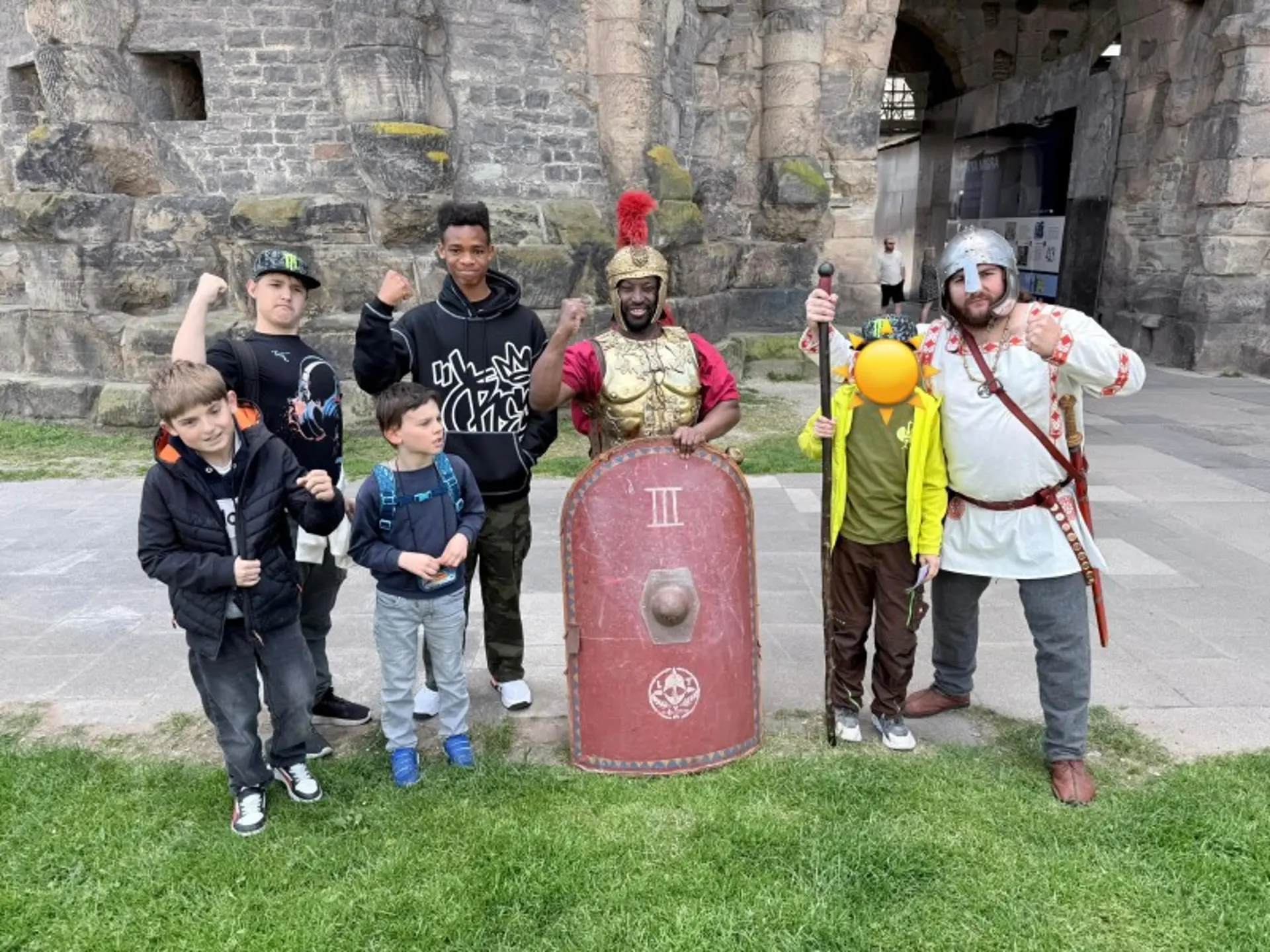 Gruppenbild vor der Porta Nigra: fünf Kinder stehen neben zwei Erwachsenen, die als römischer Gladiator und germanischer Krieger verkleidet sind.