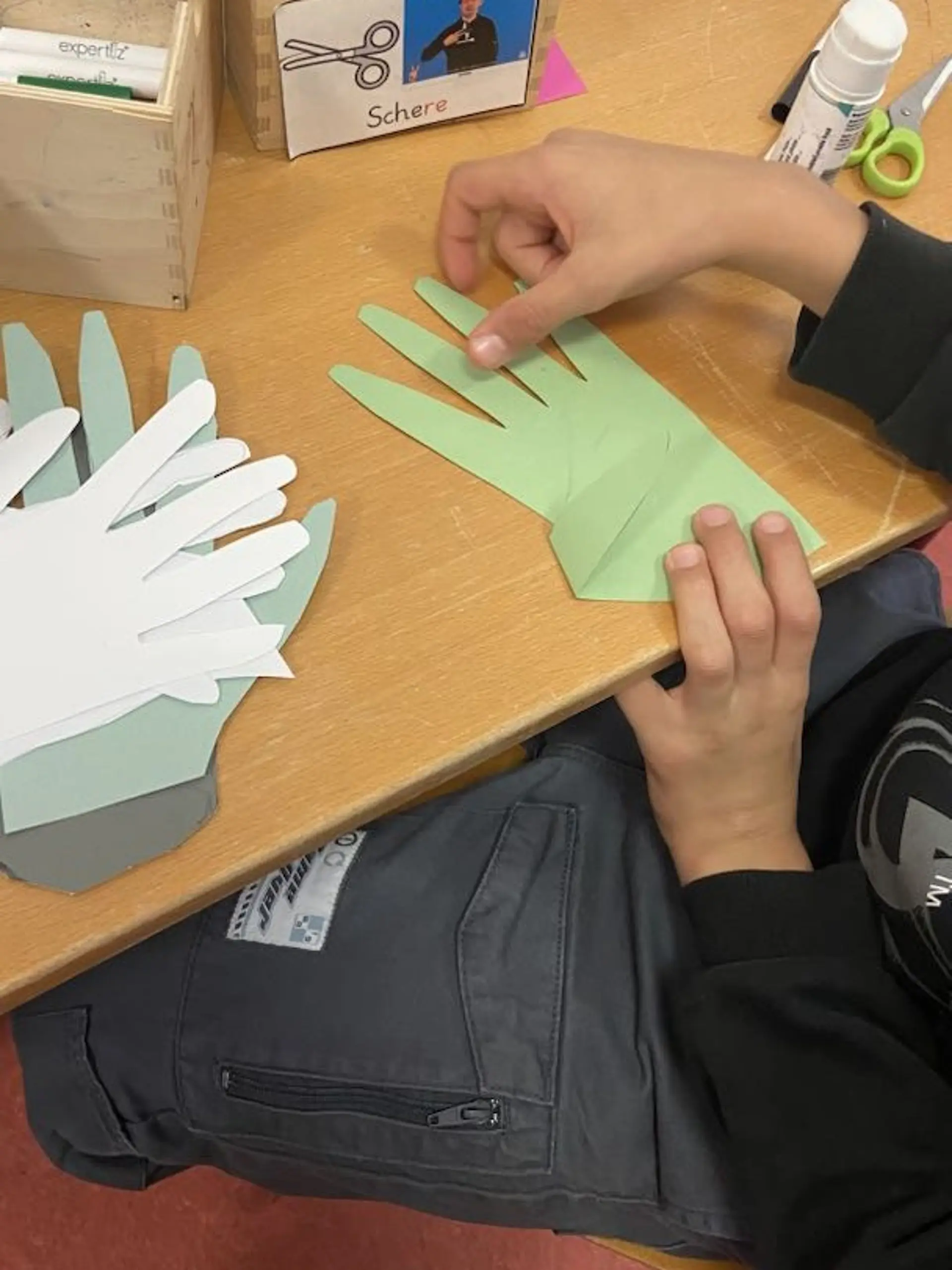 die Finger einer ausgeschnittenen hellgrünen Hand, werden zu einer Gebärde gefaltet