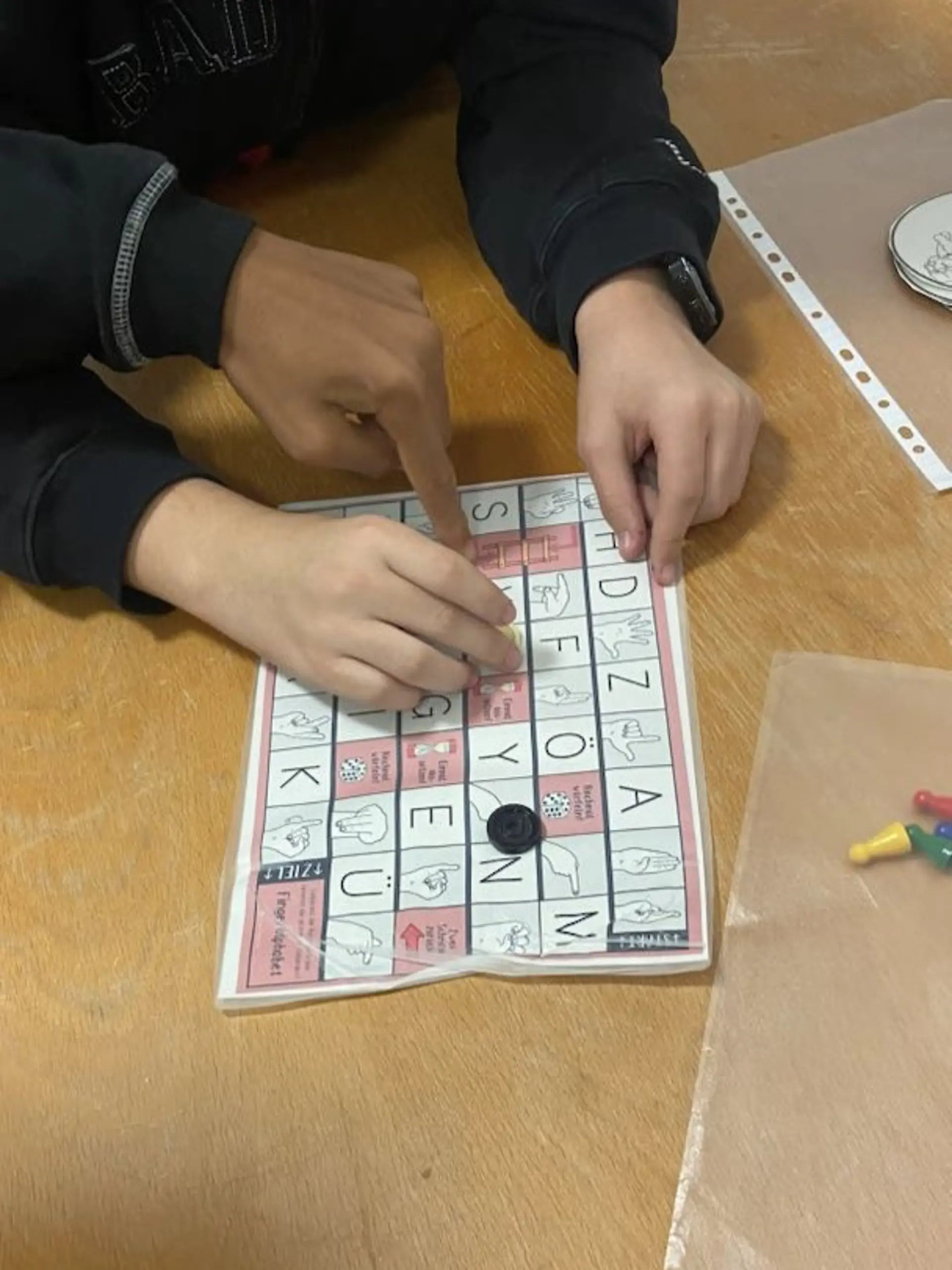 Hand liegt auf einem Spielplan mit Fingeralphabet und Buchstaben