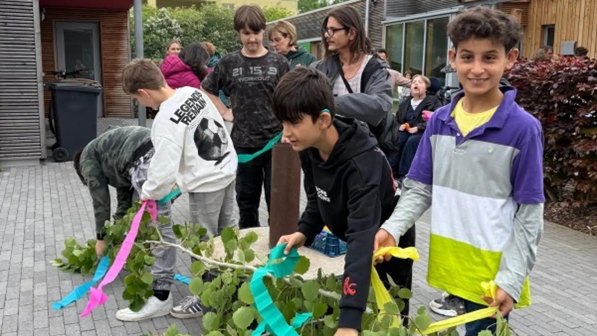 Viele Menschen schmücken gemeinsam einen Maibaum mit bunten Schleifen. Er liegt noch auf dem Boden.