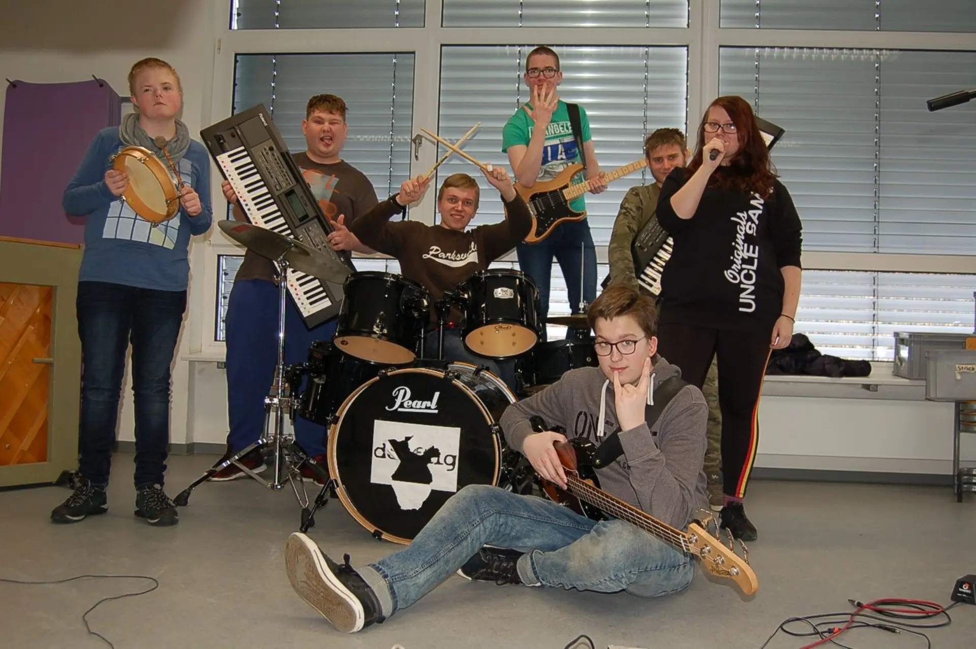 Gruppenbild der Schulband deaftig: Zwei Keyboarder, ein Schlagzeuger, zwei Bassisten, ein Junge am Tambourin und eine Sängerin