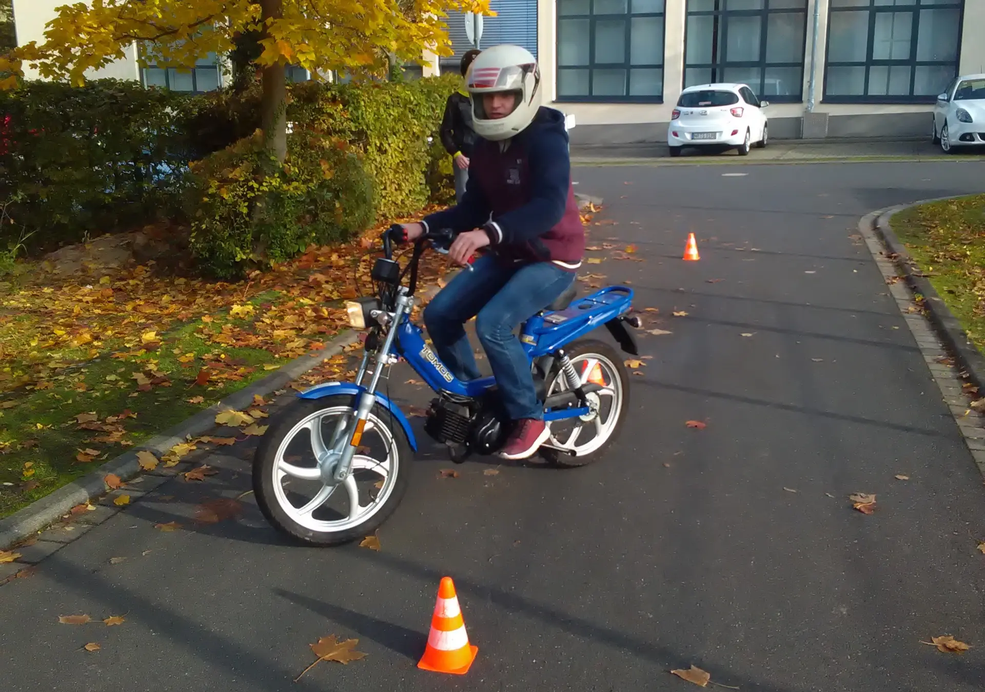 Ein Jugendlicher fährt mit einem Mofa auf einem Parkplatz um orangene Hütchen herum.