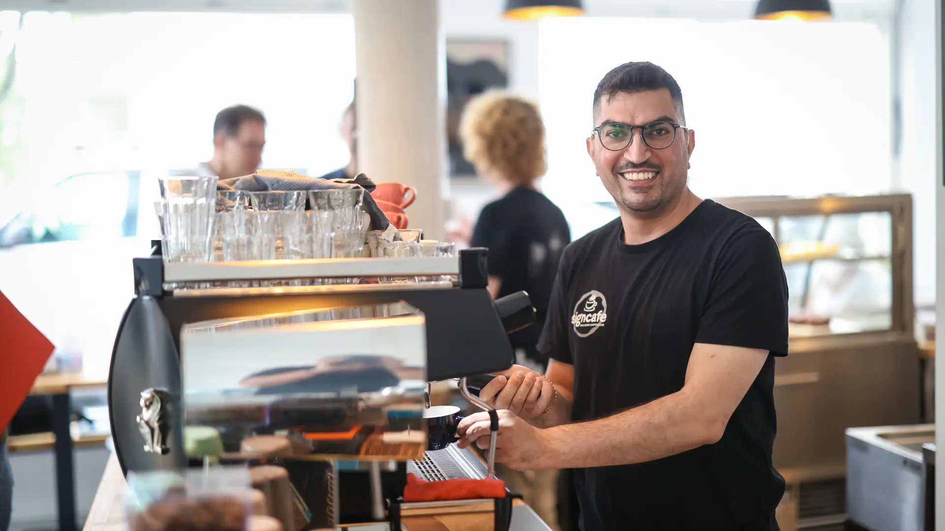 Bild zeigt den Barista im signcafé, der an der Cafétheke freundlich lächelt. 