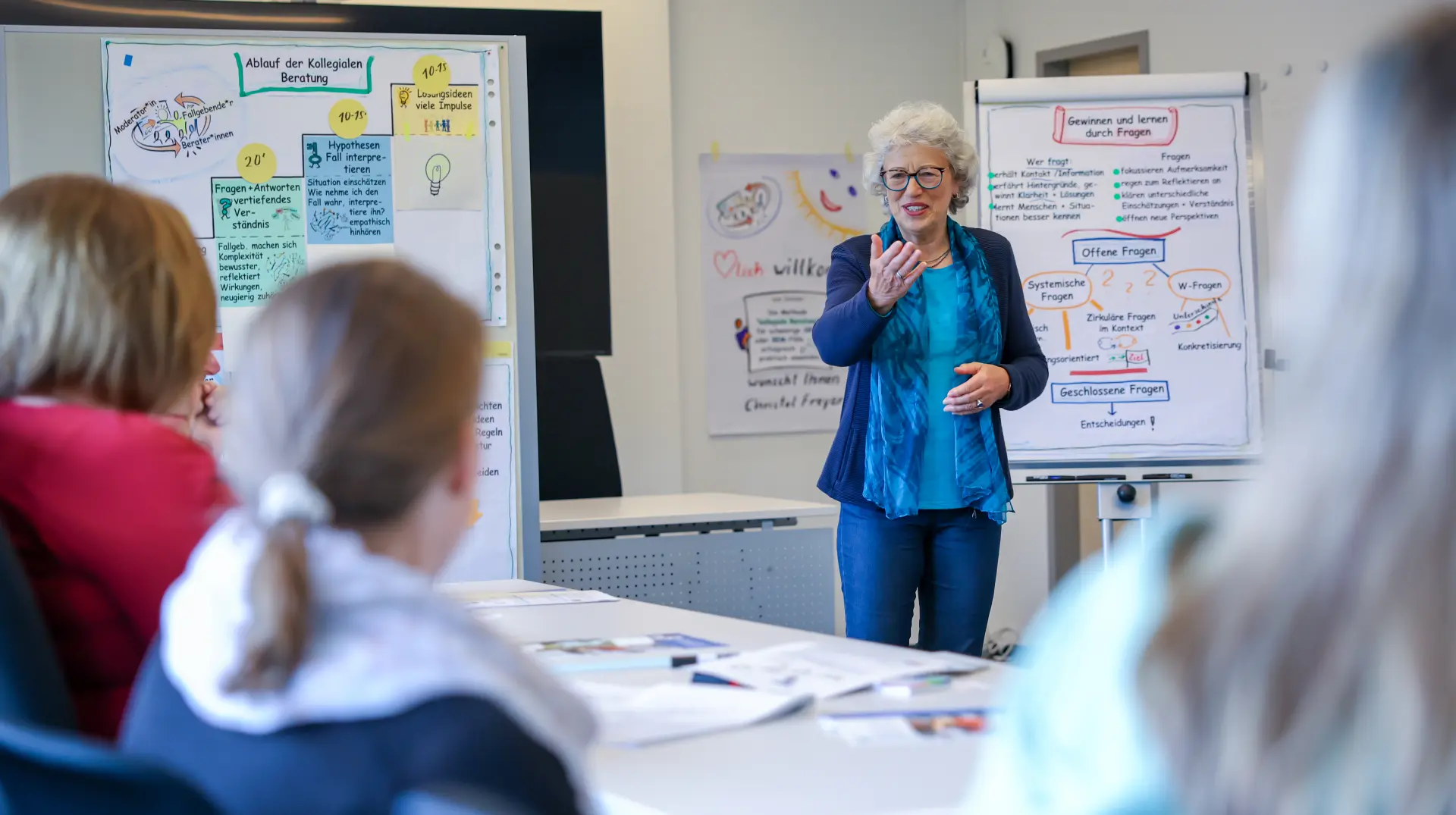 Eine Referentin spricht vor Seminarteilnehmenden und im Hintergrund sind beschriftete Flipcharts zu sehen.