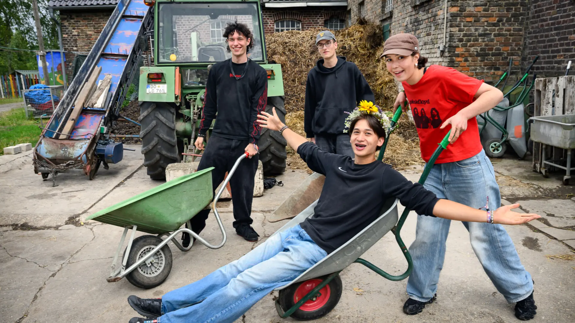 Vier Freiwillige lachen in die Kamera. Einer wird in einer Schubkarre geschoben.
