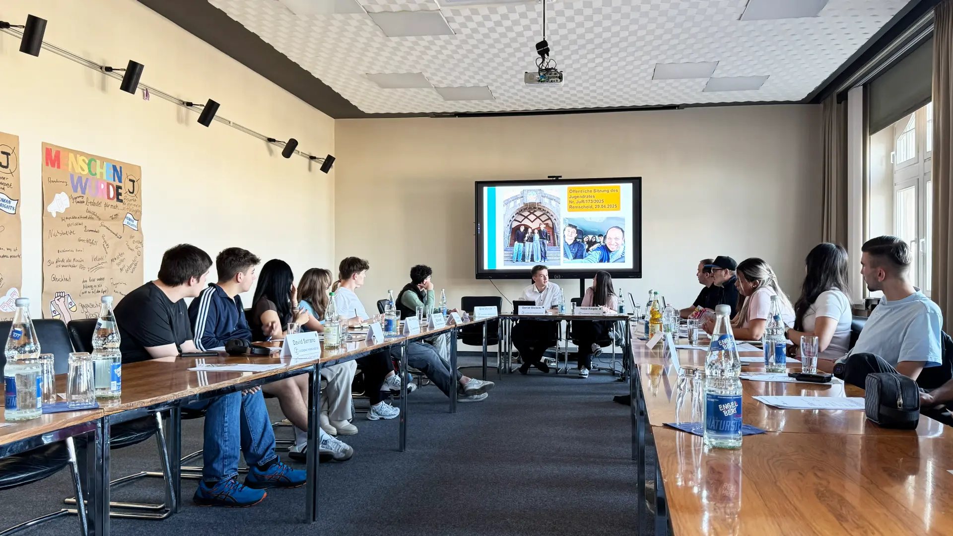 Jugendliche sitzen an einem langen Tisch und schauen auf eine Präsentation