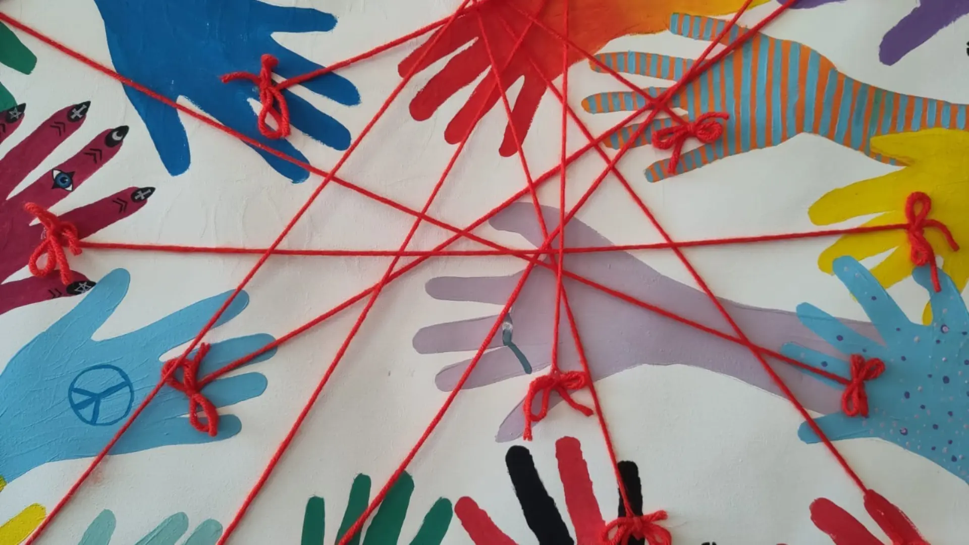 bunte gemalte Hände, die mit roten Wollfäden miteinander verbunden sind