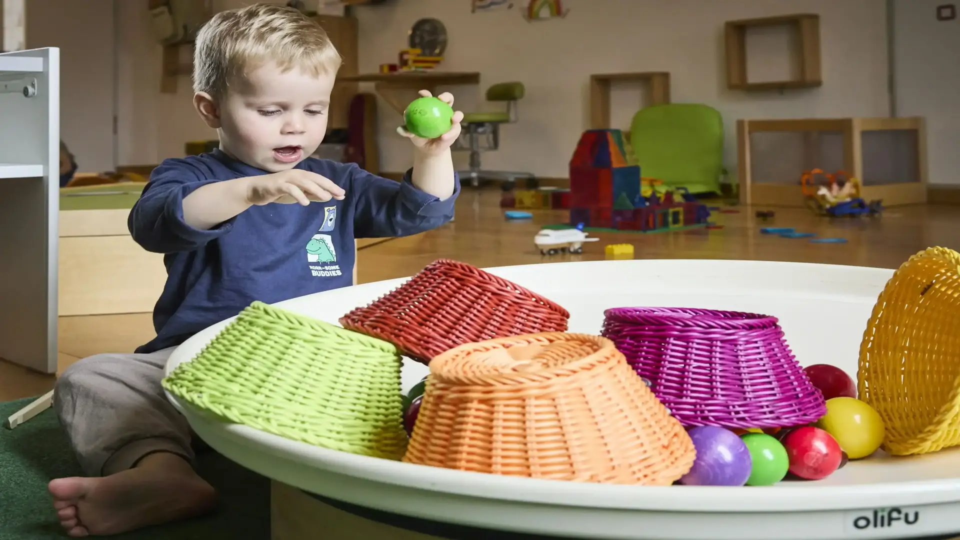 Ein Kind sitzt auf dem Boden und spielt mit Bällen und bunten Körben.