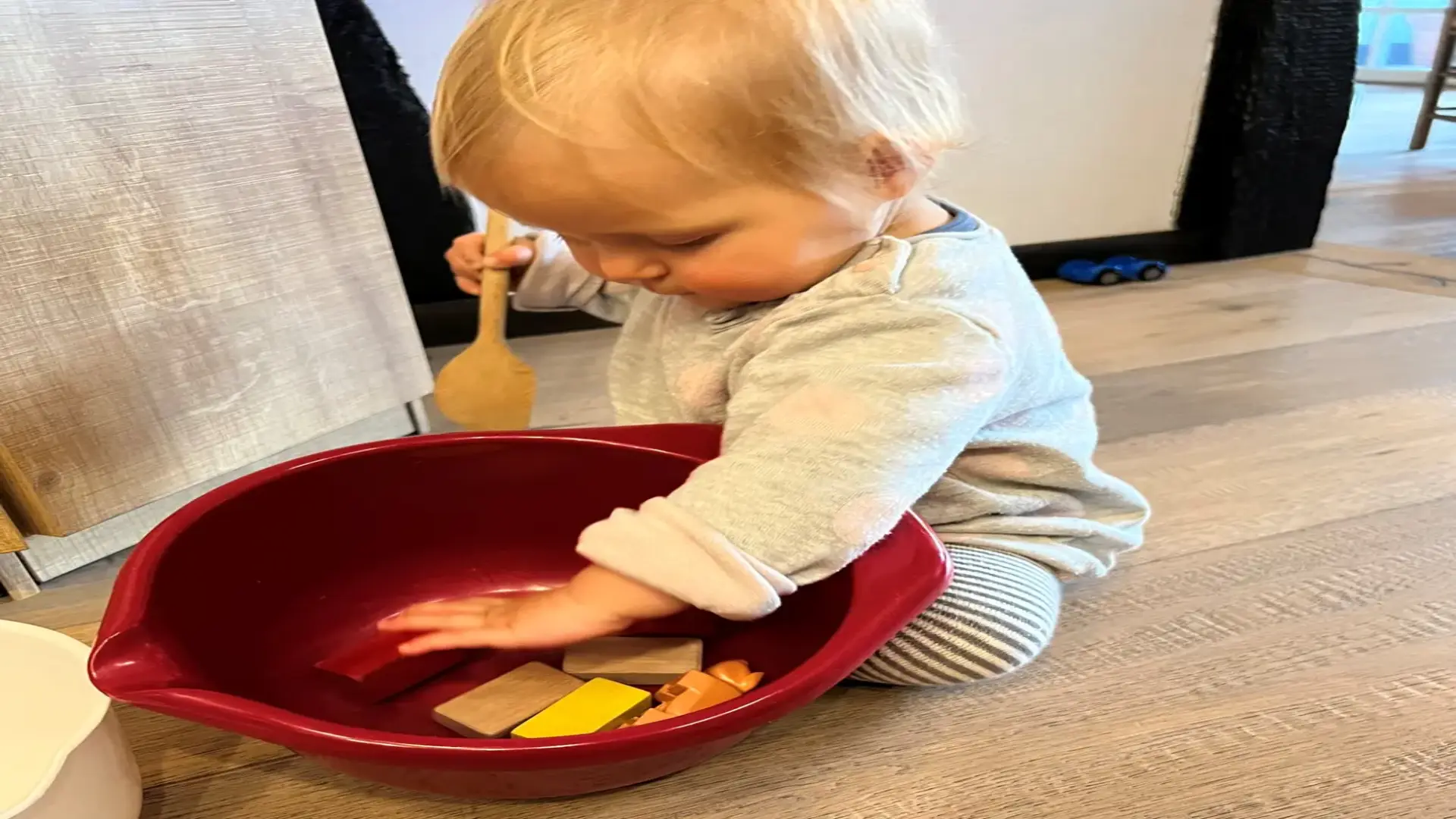 Ein Kind sitzt auf dem Boden und spielt mit Holzklätzen und einem Kochlöffel.