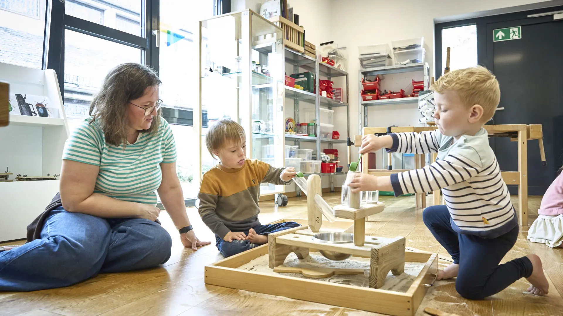 Kinder spielen in einer Kita, eine Erzieherin sitzt daneben. 