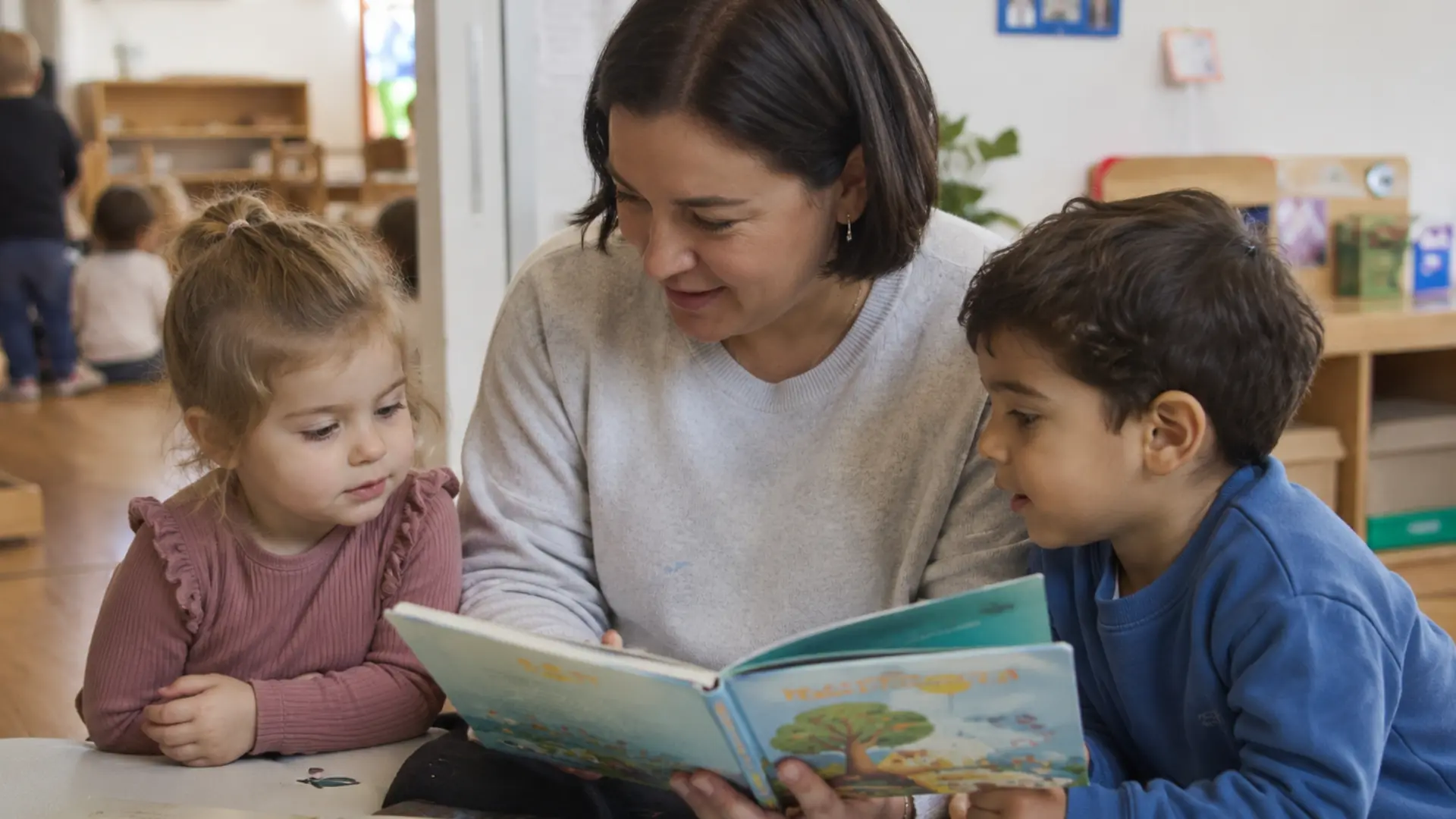 Eine Erzieherin liest mit zwei Kindern in einem Buch.