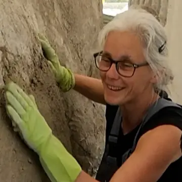 Eine Frau mit Brille trägt Gummihandschuhe und betoniert eine Skulptur.