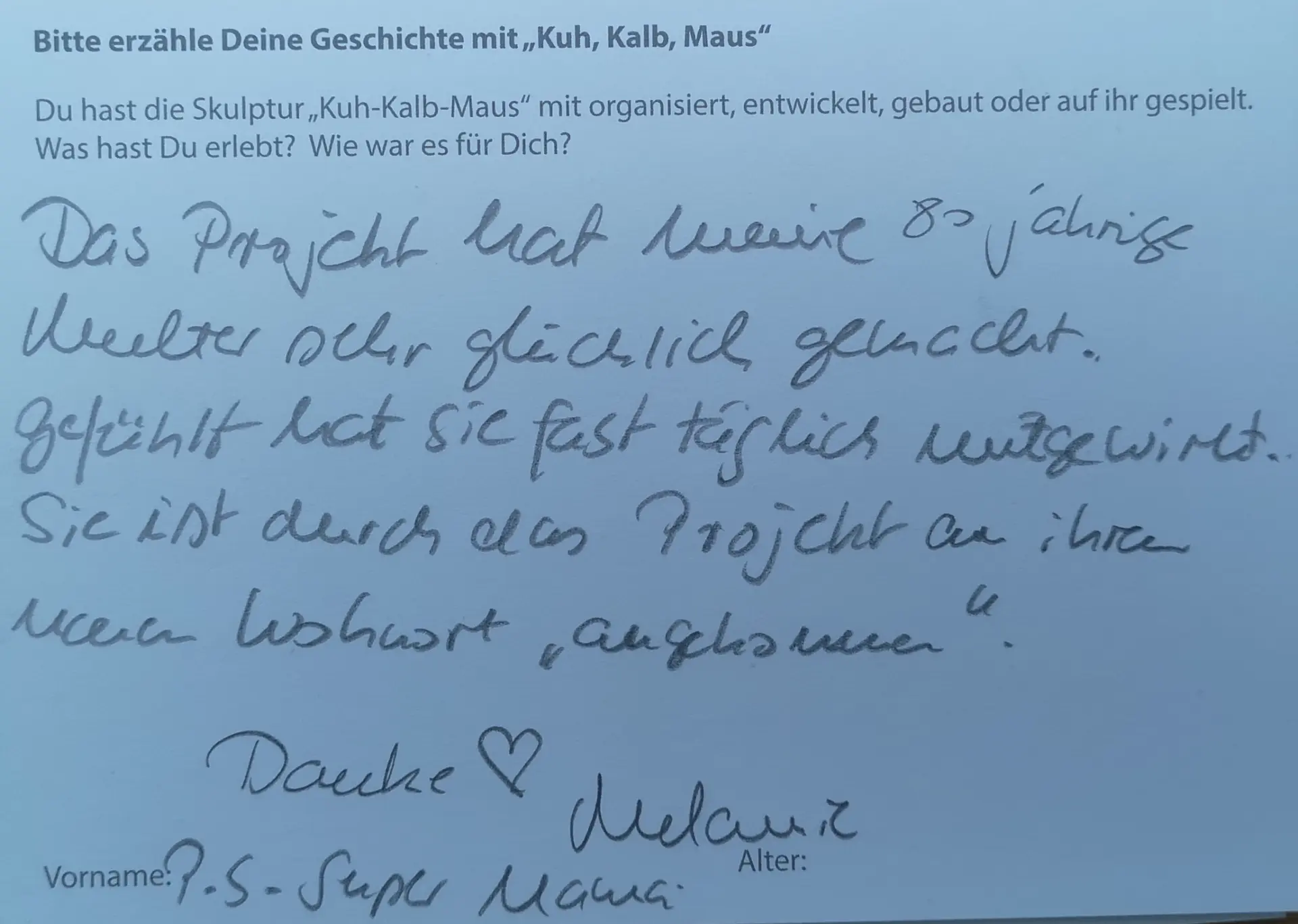 Eine Karte mit der Aufforderung: Bitte erzähle Deine Geschichte mit "Kuh, Kalb, Maus. Du hast die Skulptur "Kuh, Kalb, Maus" mit organisiert, entwickelt, gebaut oder auf ihr gespielt. Was hast Du erlebt? Wie war es für Dich? Antworttext: Rückmeldekarte einer Teilnehmerin: "Das Projekt hat meine 80-jährige Mutter sehr glücklich gemacht. Gefühlt hat sie fast täglich mitgewirkt. Sie ist durch das Projekt an ihrem neuen Wohnort 'angekommen'. Danke, Melanie. P.S. Super Mama.