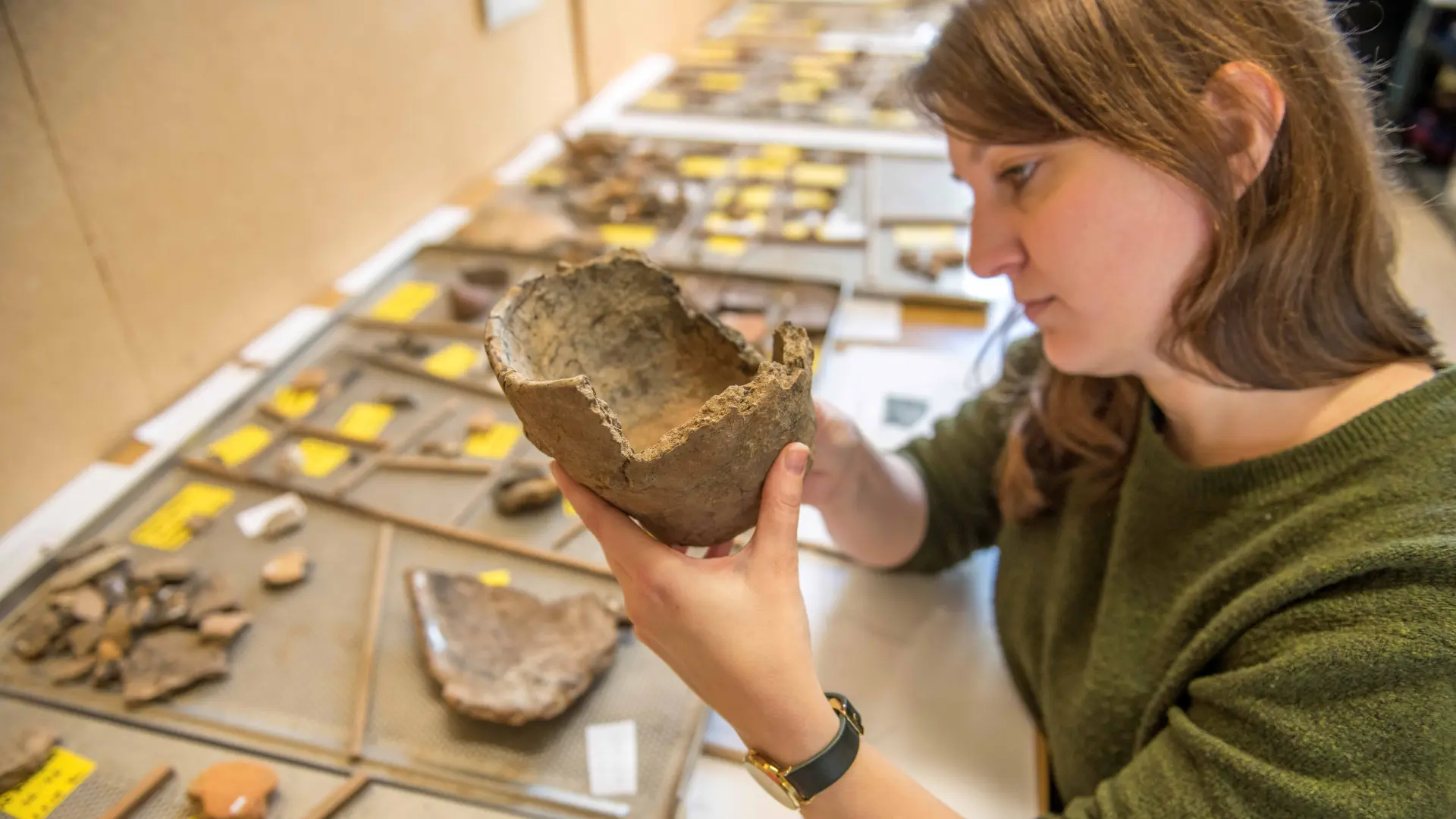 Foto: eine junge Frau untersucht einen archäologischen Fund.