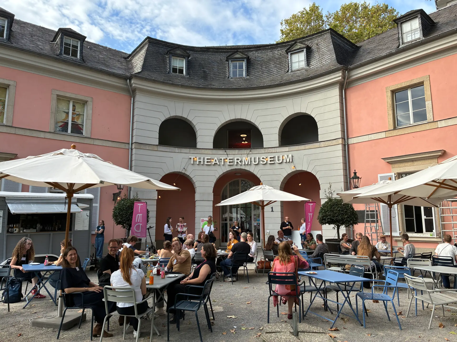 Foto: Die Teilnehmenden sitzen in der Pause des rheinforUm draußen vor dem Theatermuseum und führen Gespräche.