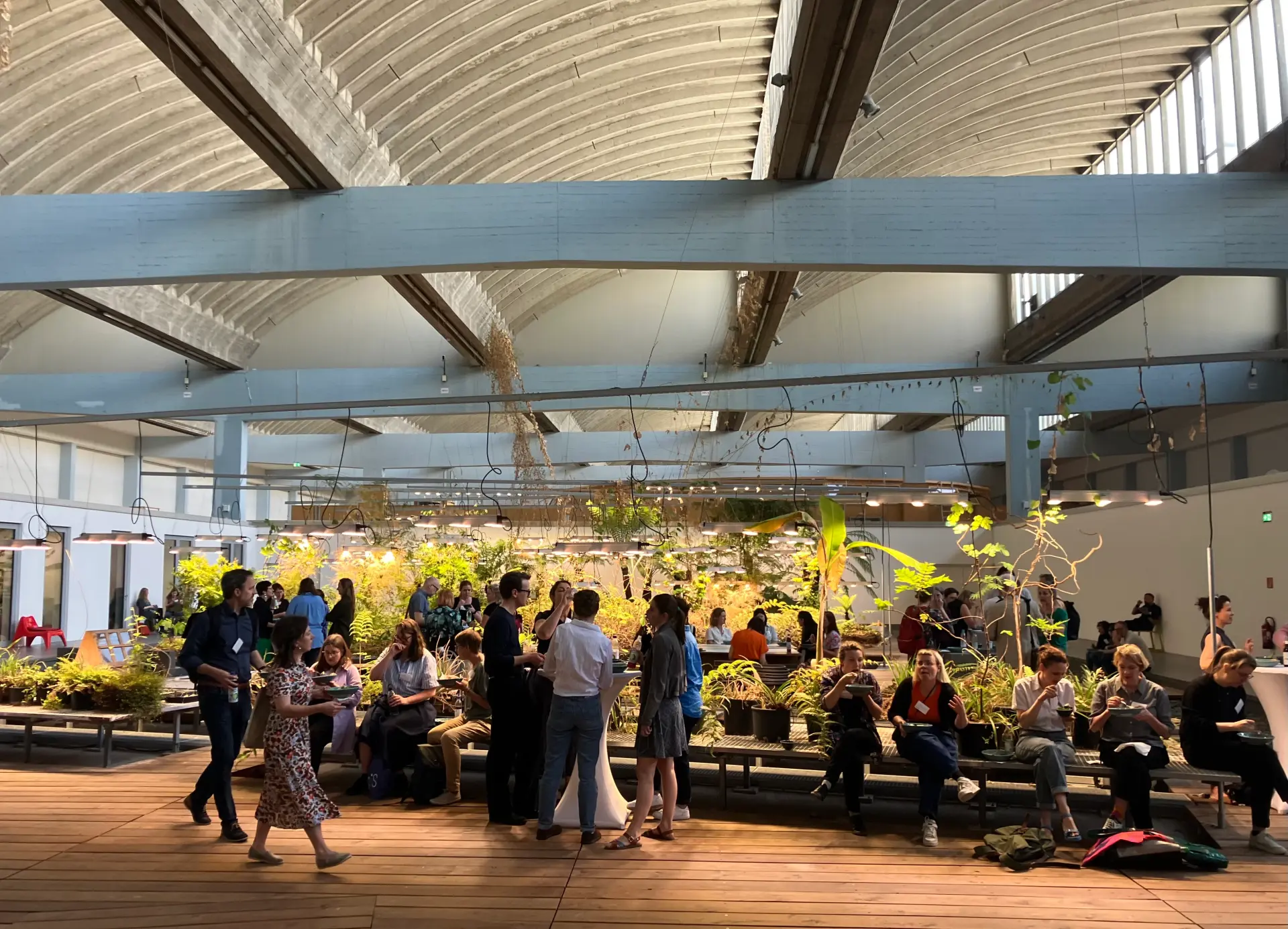 Foto: Teilnehmende der MAI-Tagung unterhalten sich während der Pause in er W. Michael Blumenthal Akademie des Jüdischen Museums Berlin. Im Hintergrund ist der grünbepflanzte "Diaspora- Garten" zu sehen.