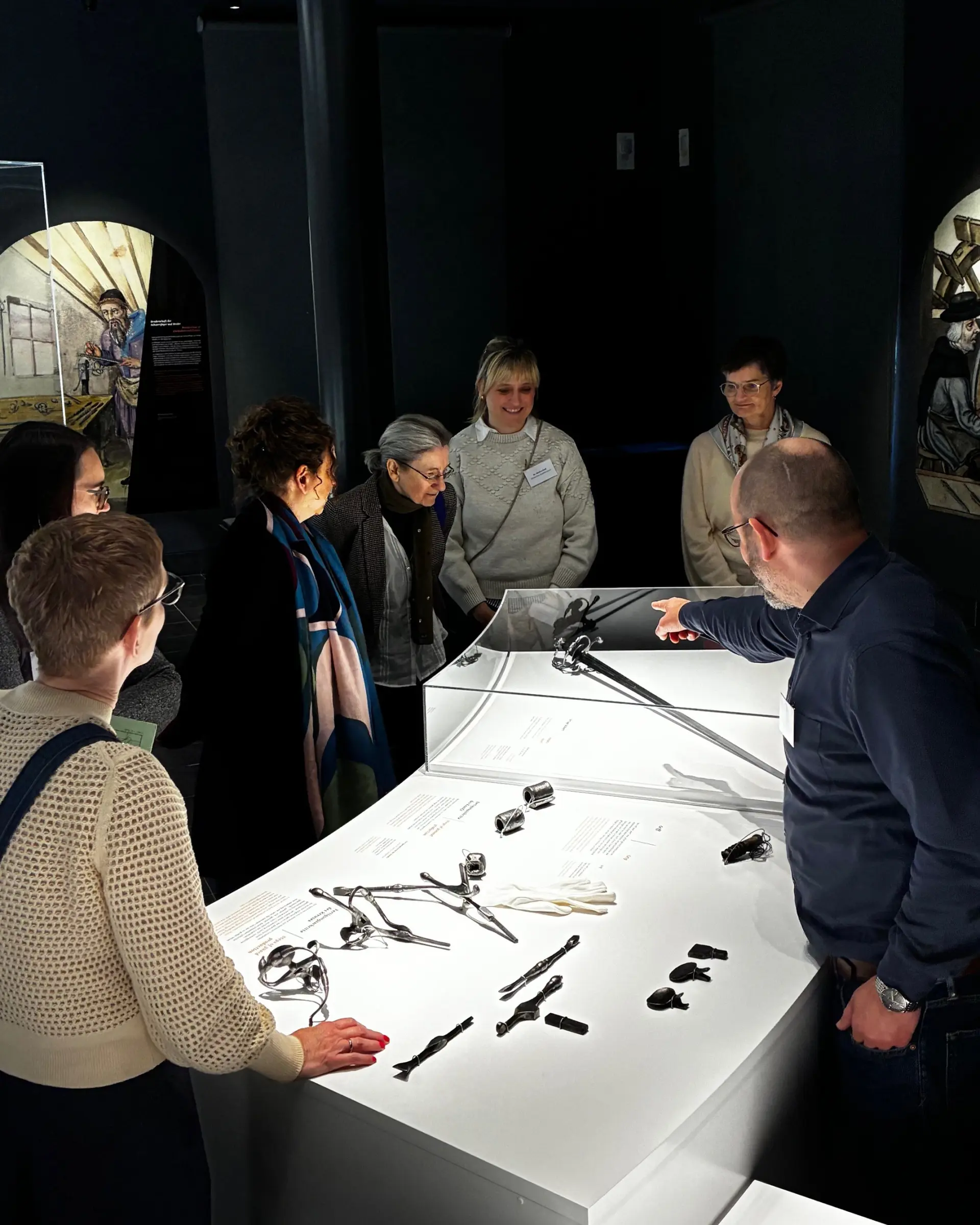 Eine Gruppe Museumsbesuchender Blicken auf einen Ausstellungobjekte in einer Vitrine. U.a. ist ein Säbel zu sehen auf welchen der Museumsdirektor Sixt Wetzler zeigt und etwas dazu erläutert.