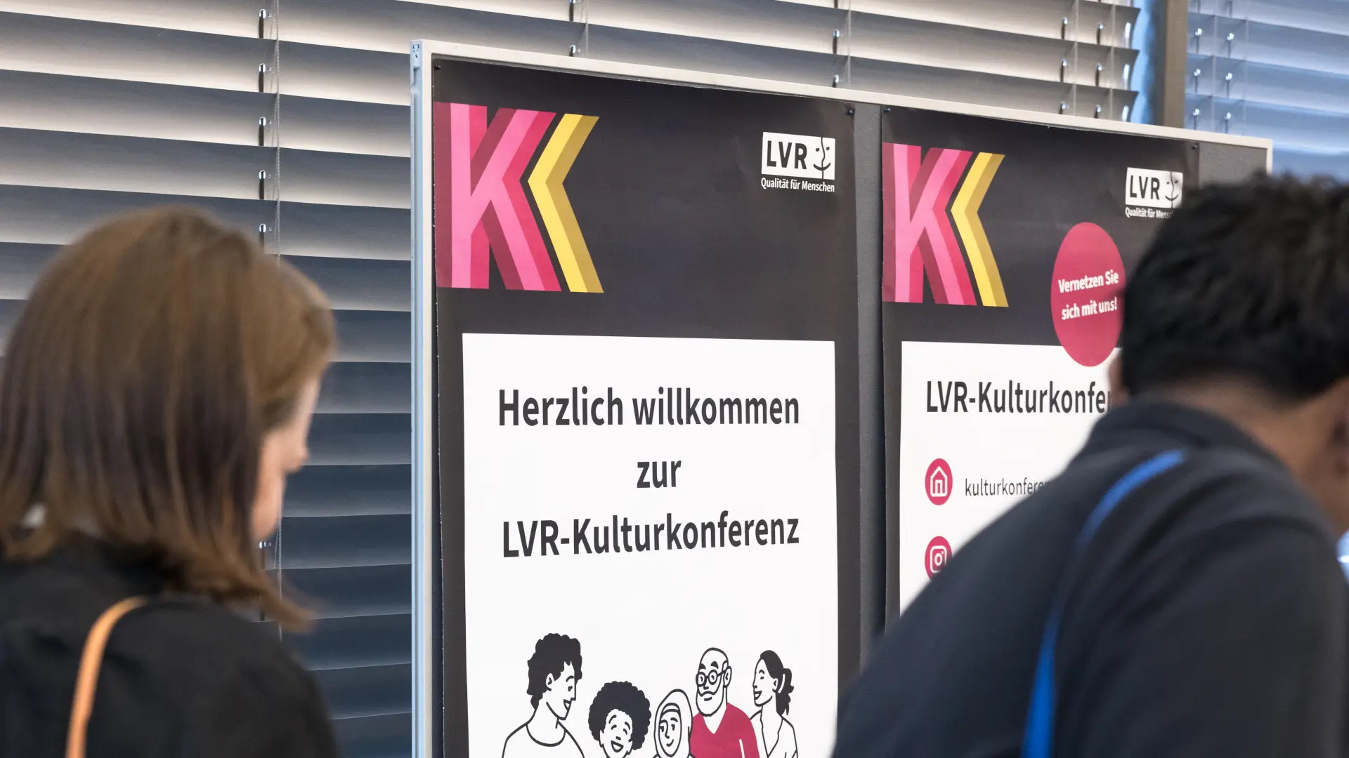 Mehrere Personen stehen auf einer Bühne vor einem Publikum in einem großen Raum mit Skulpturen und einem Bildschirm.