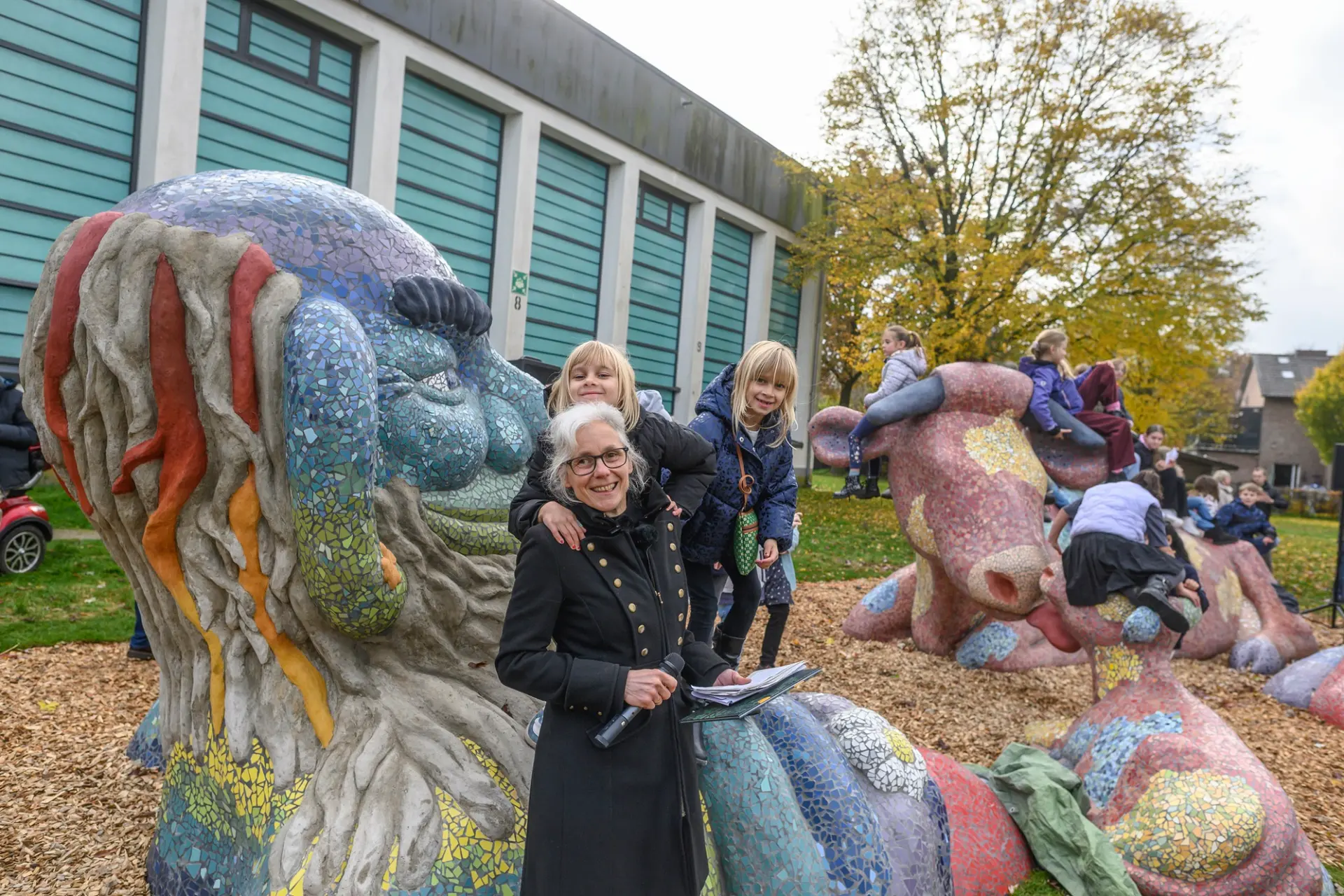 Foto: Eine Gruppe von Menschen sitzt auf einer Großskulptur bestehend aus Riese, Kuh und Kalb.