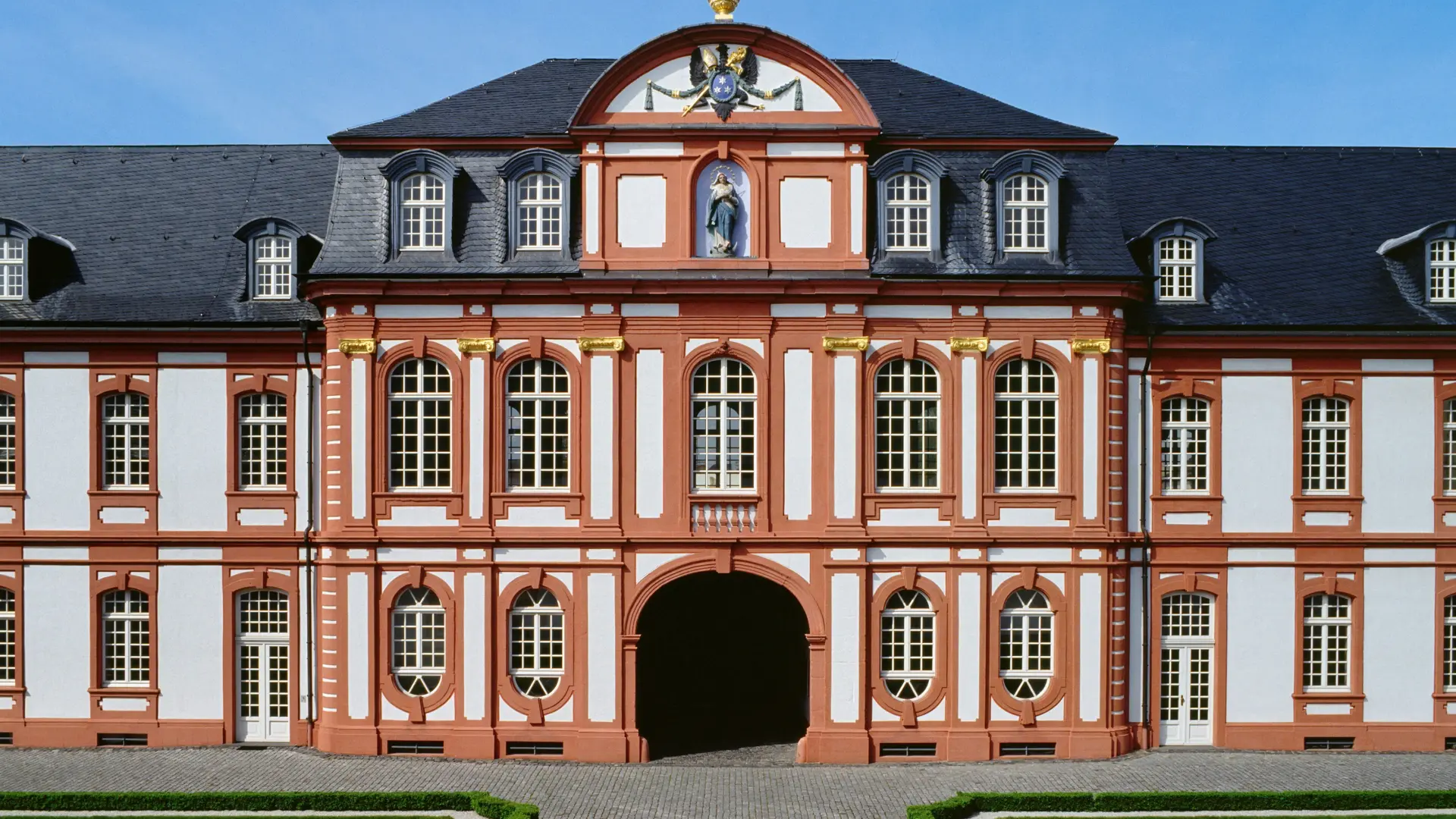 Foto: Ein prächtiges altes Gebäude aus weißen und roten Steinen mit vielen Fenstern und einem großen Eingangstor