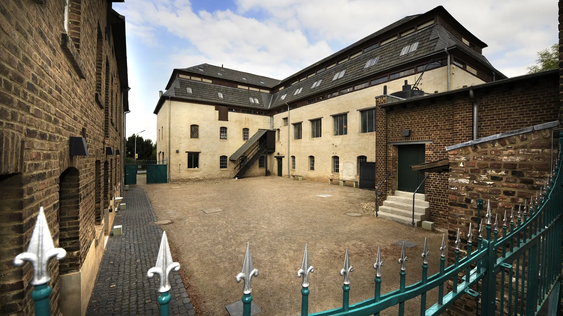 Foto: Fabrikgebäude mit Innenhof und einem Zaun