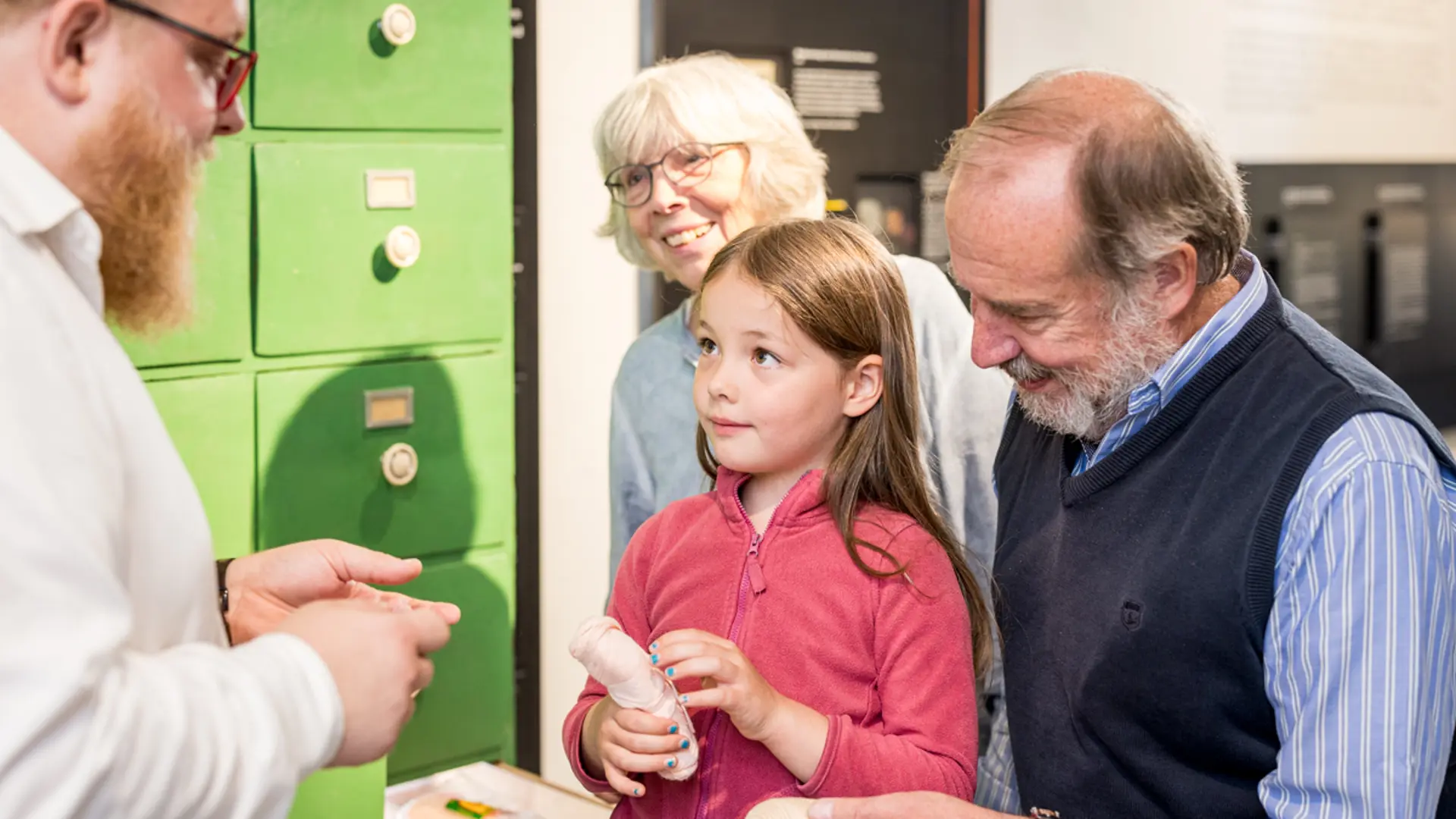 Foto: Ein Museumsmitarbeiter spricht mit einem Mädchen und ihren Großeltern 