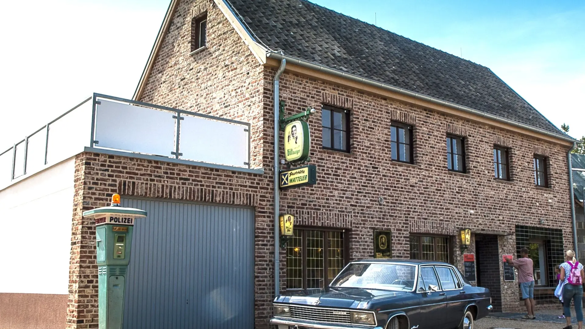 Foto: Großes Gebäude aus rotem Bachstein mit einem historischen PKW im Vordergrund