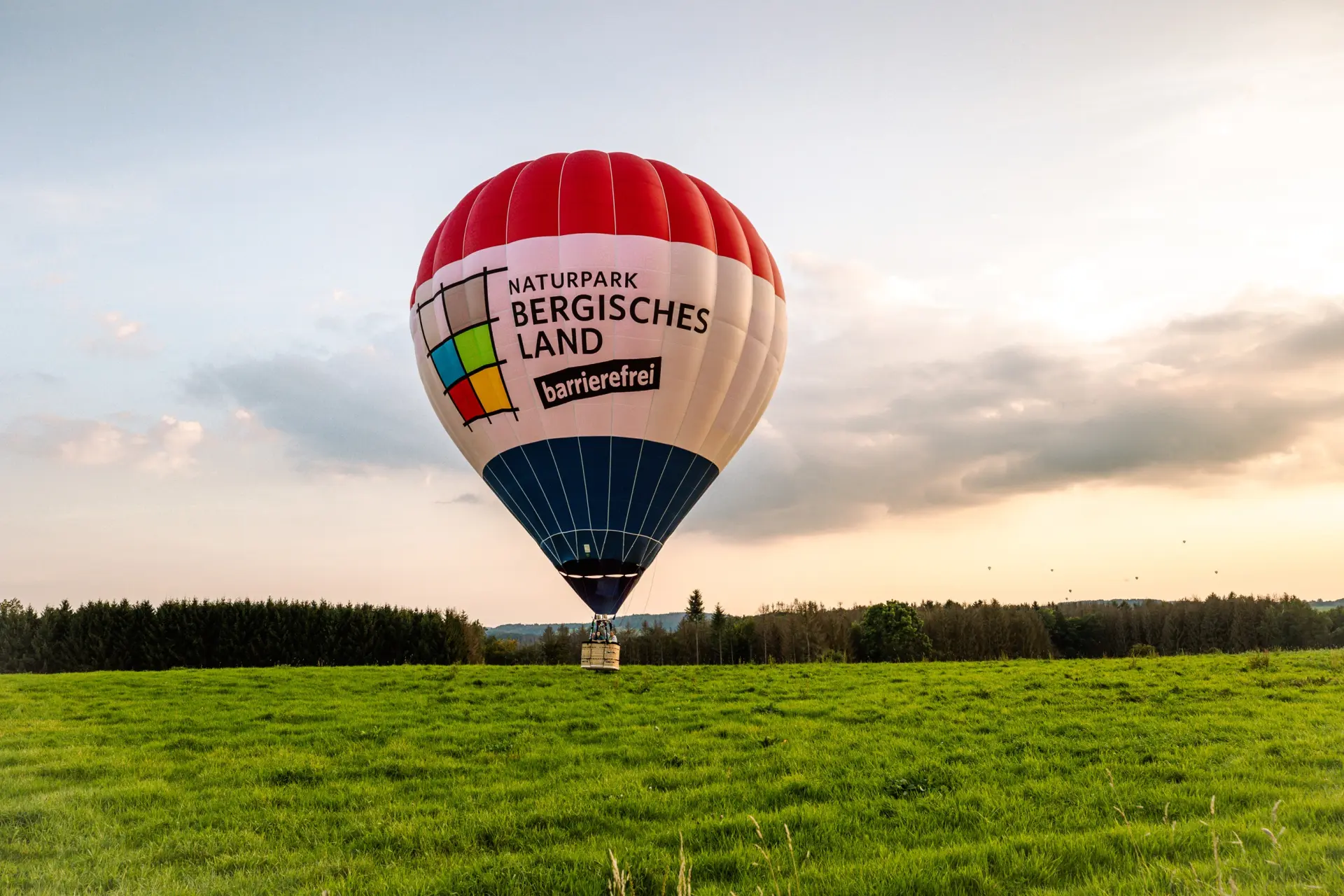 Heißluftballon in abendelicher Stimmung landet auf einer grünen Wiese