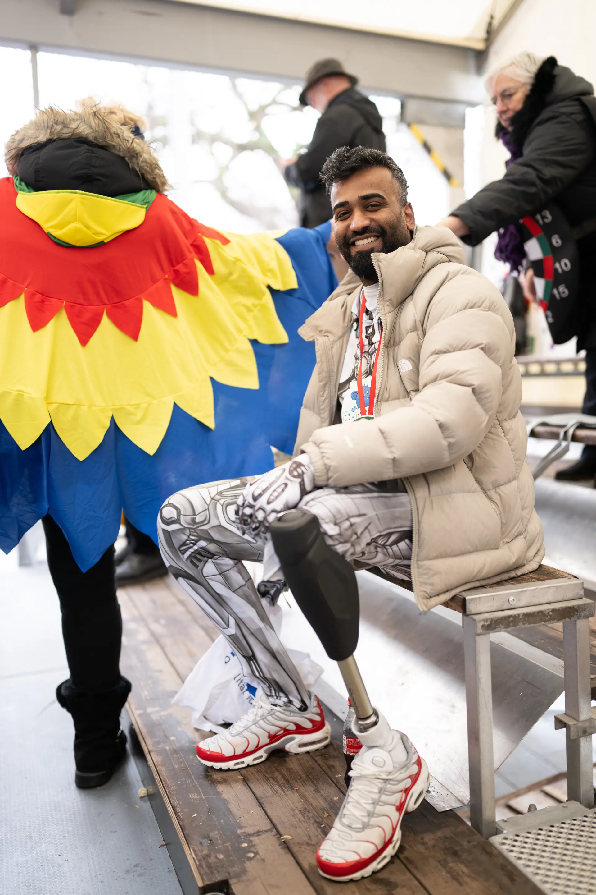 Ein Mann mit zwei Bein-Prothesen sitzt lächelnd auf einer Bank beim Düsseldorfer Rosenmontagszug.