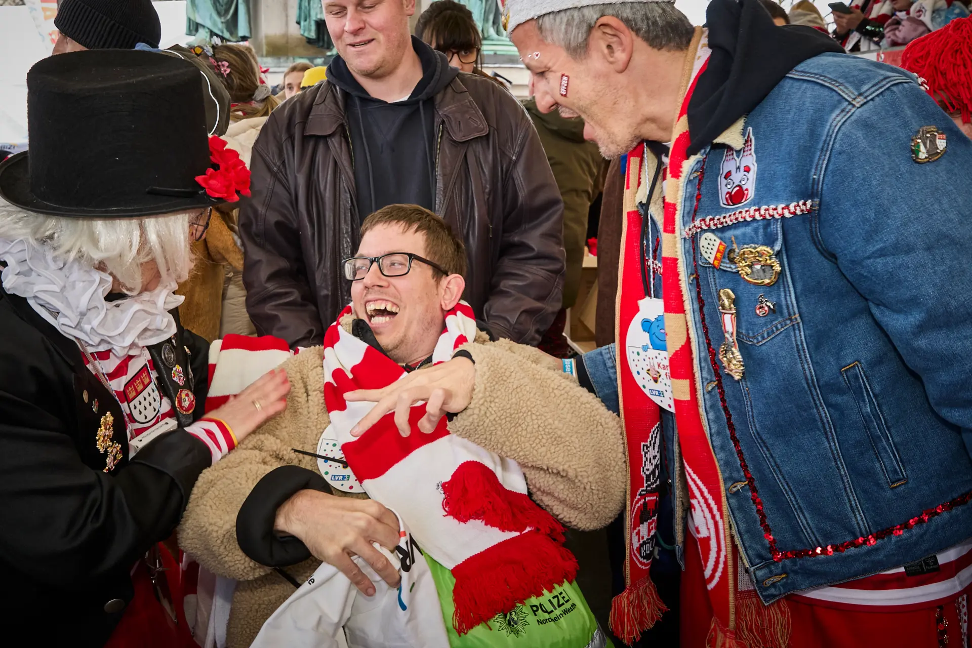 Ein Mann im Rollstuhl unterhält sich gut gelaunt mit anderen feiernden Menschen beim Kölner Rosenmontagszug.