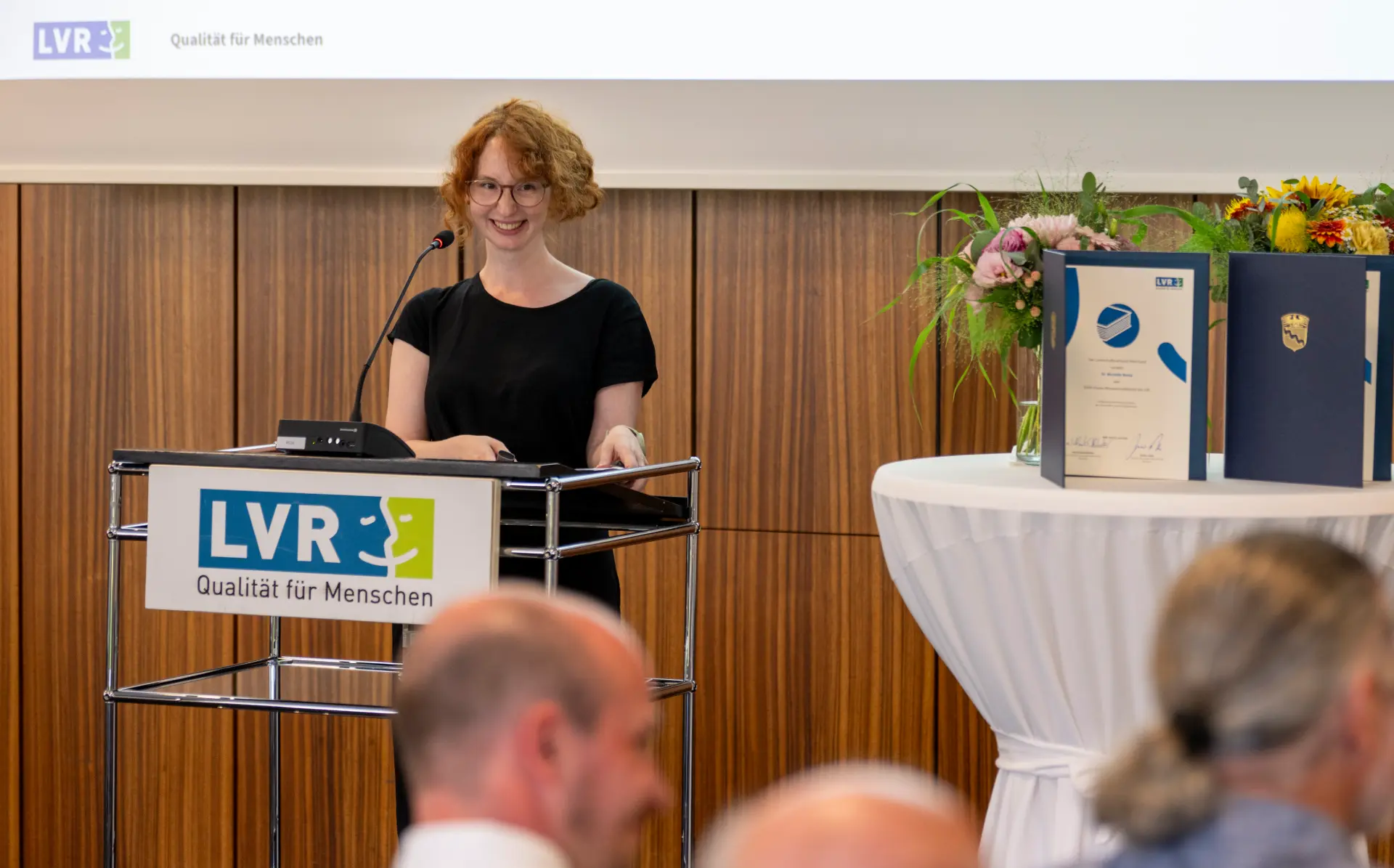 Eine Frau in einer schwarzen Bluse steht an einem Rednerpult.