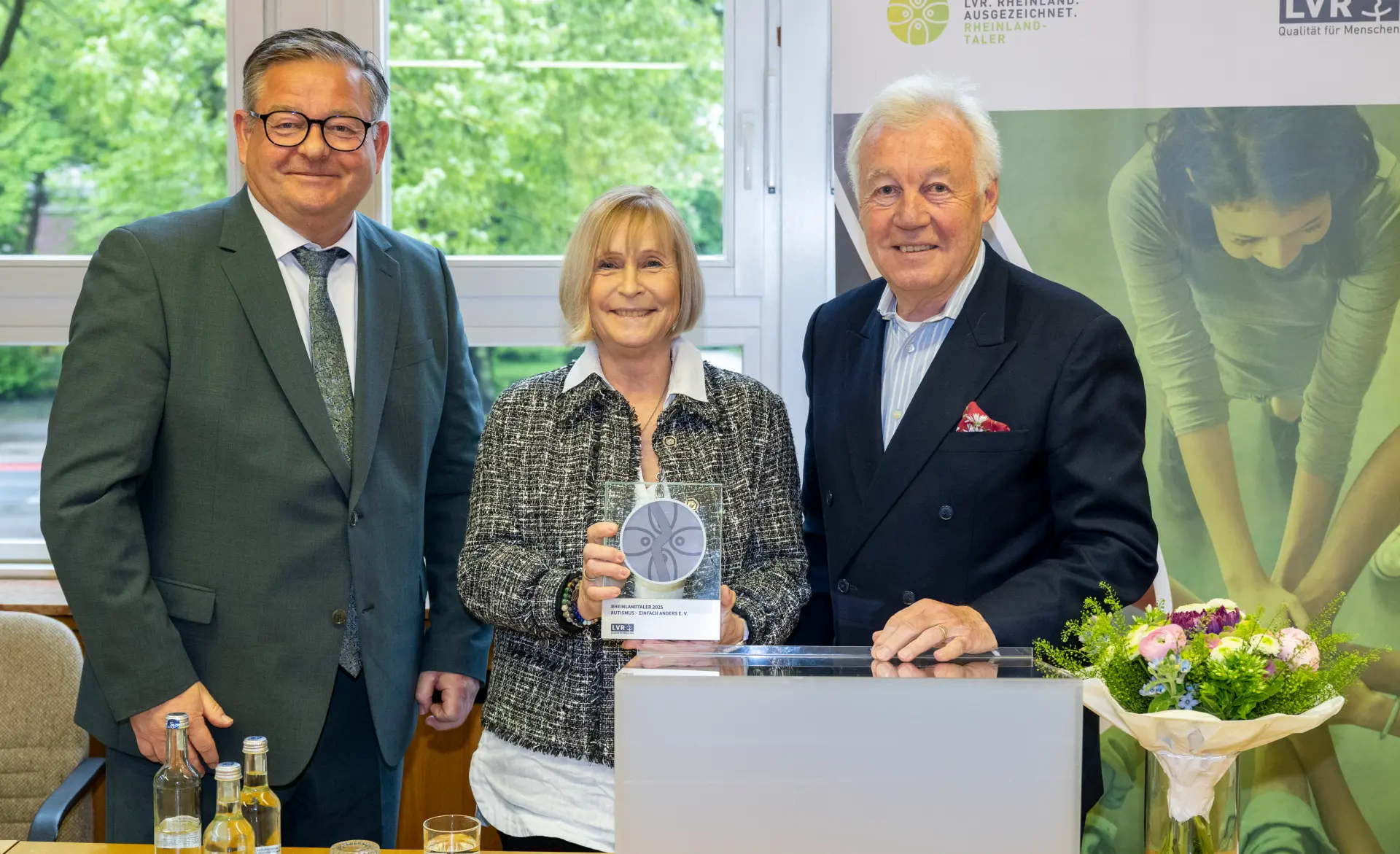 Zwei Männer und eine Frau. Die Frau in der Mitte hält eine Trophäe.