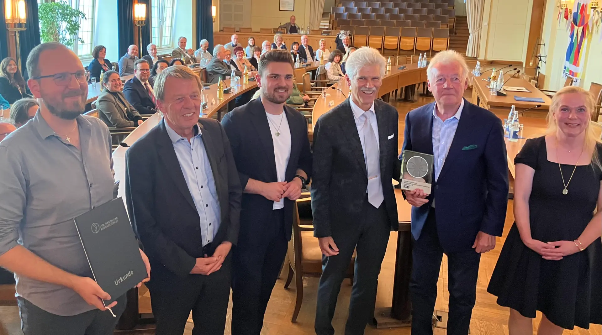 Ein Gruppenfoto in einem Saal. Der zweite Mann von rechts hält eine Trophäe in der Hand.