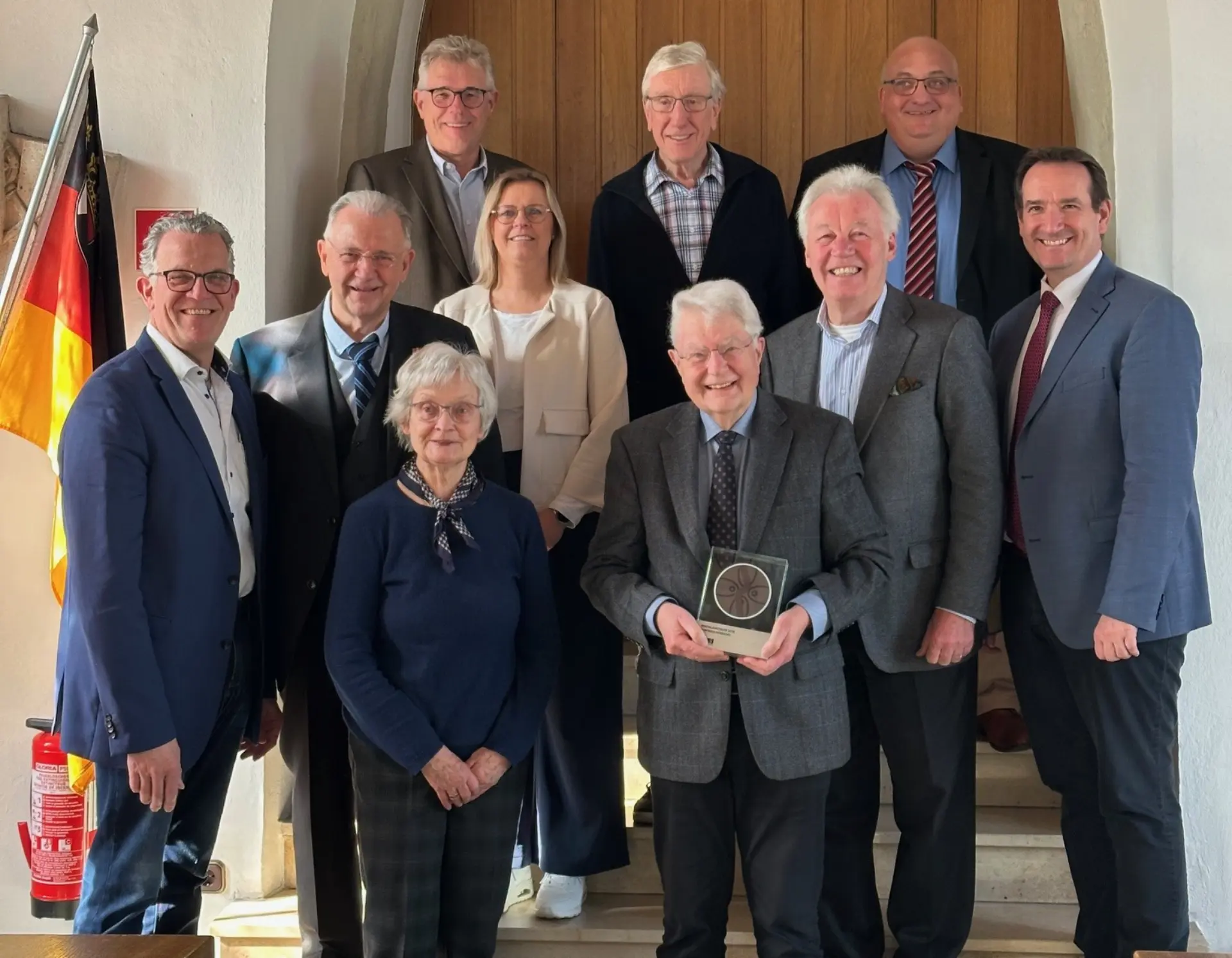 Ein Gruppenfoto vor einer Holztür. Der Mann vorne in der Mitte hält eine Trophäe in der Hand.