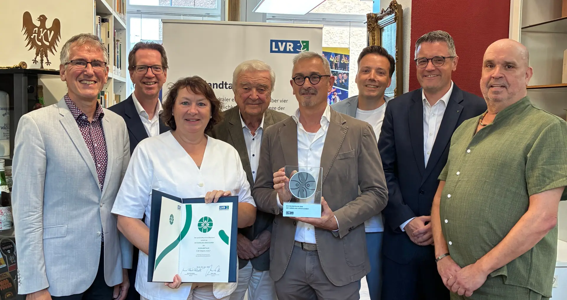 Ein Gruppenfoto. Eine Frau hält eine Urkunde in der Hand, eine Mann daneben eine Trophäe.