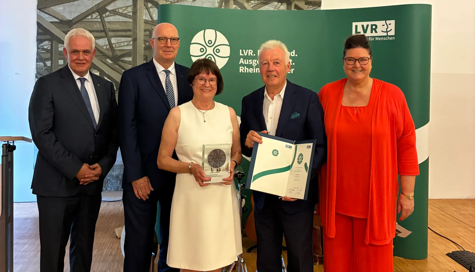 Eine Gruppe Menschen lächelt in die Kamera. Die Frau in der Mitte hält eine Trophäe in der Hand.