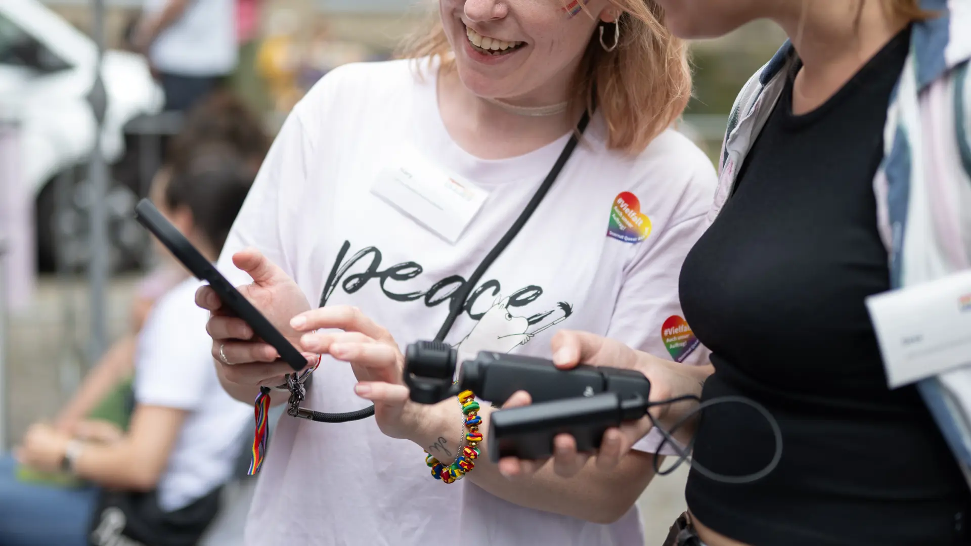 Eine Frau mit Regenbogenfächer begleitet einen weiß gekleideten Mann mit Langstock, der dem Publikum zuwinkt. Eine Grafik trägt den Text: „CSD-Inklusionsarea 2026: Ein voller Erfolg!“