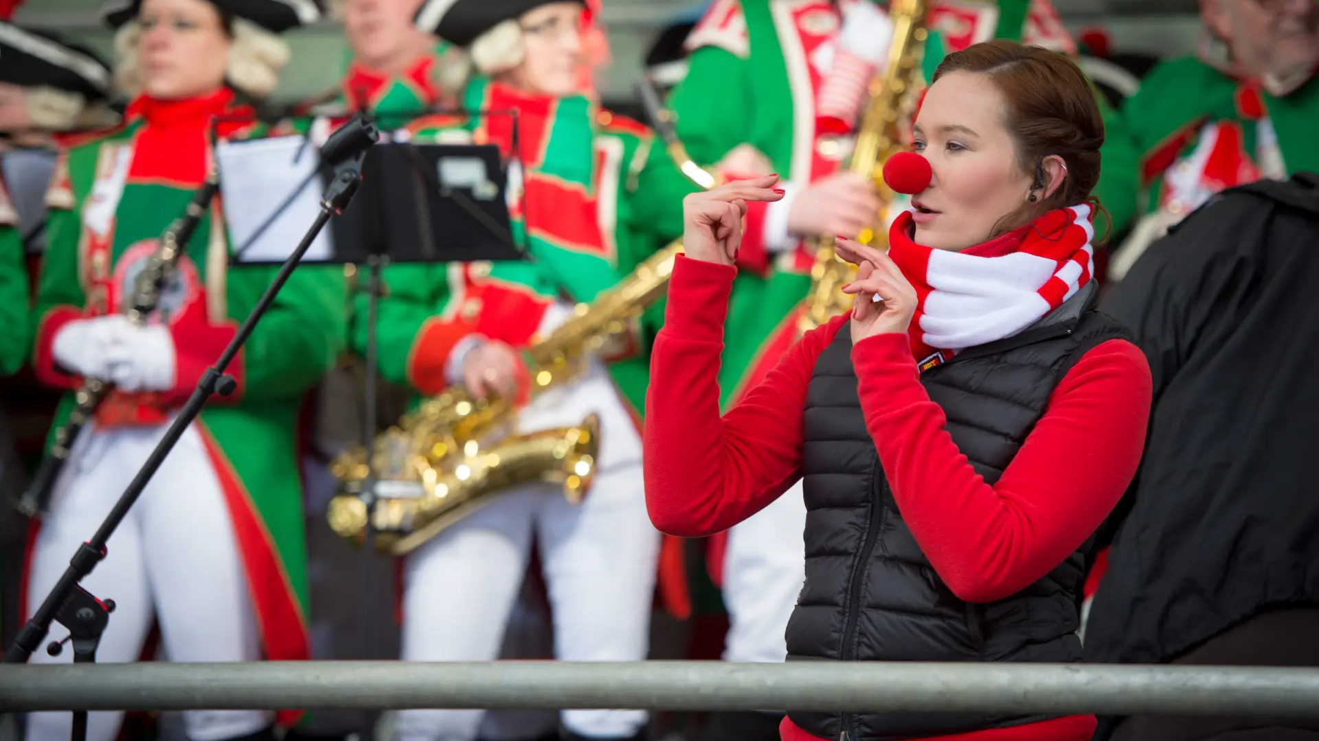 Eine Gebärdendolmetscherin überträgt das Bühnengeschehen in die Deutsche Gebärdensprache. Sie trägt eine rote Clownsnase. Im Hintergrund spielt eine Band. 