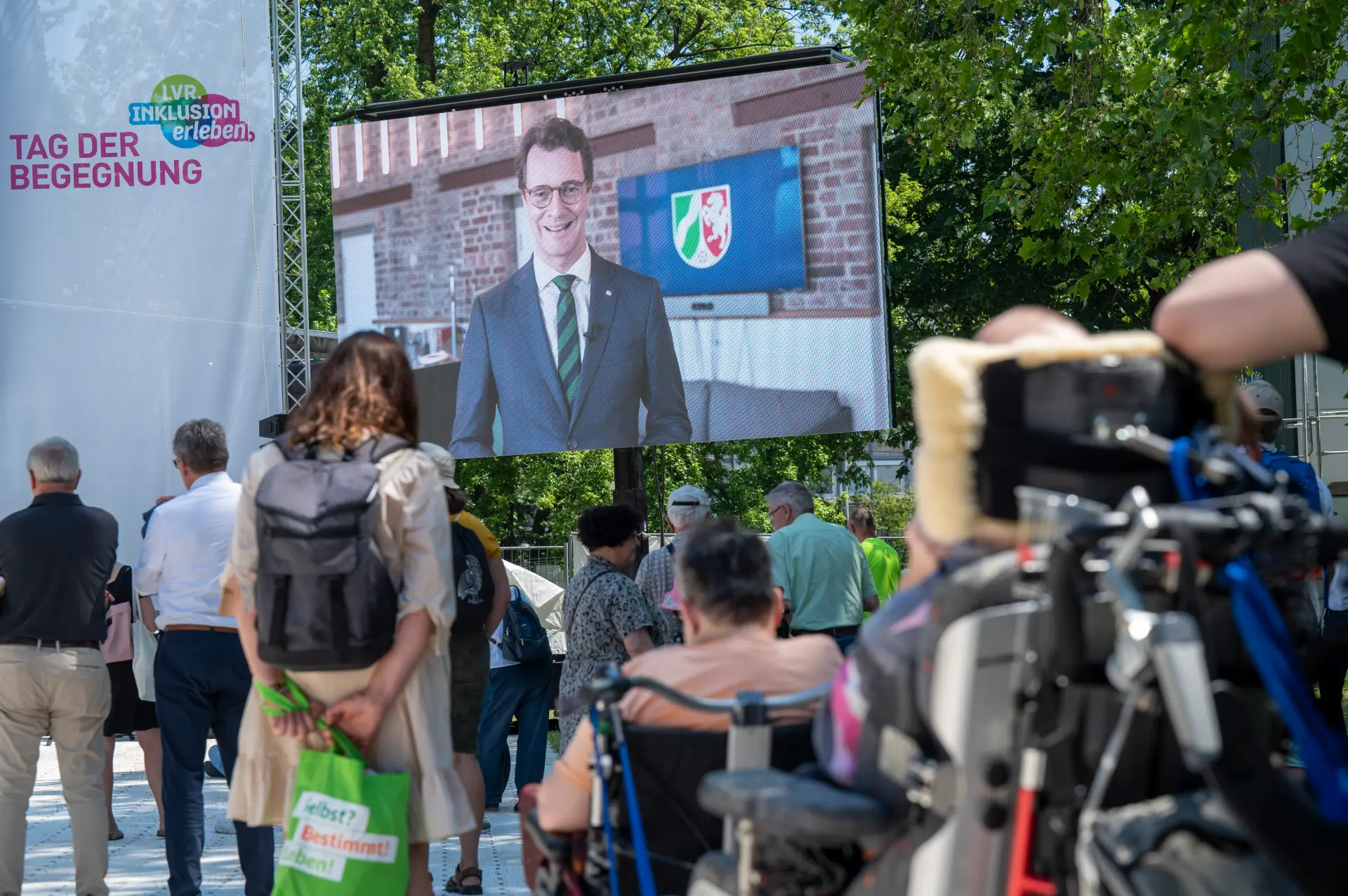 Der Ministerpräsident des Landes Nordrhein-Westfalen ist auf einer Leinwand zu sehen. Er begrüßt die Gäste des "Tags der Begegnung"