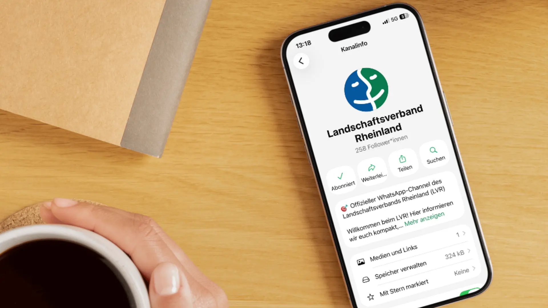 WhatsApp-Kanal des Landschaftsverbands Rheinland auf einem Smartphone neben einer Kaffeetasse.
