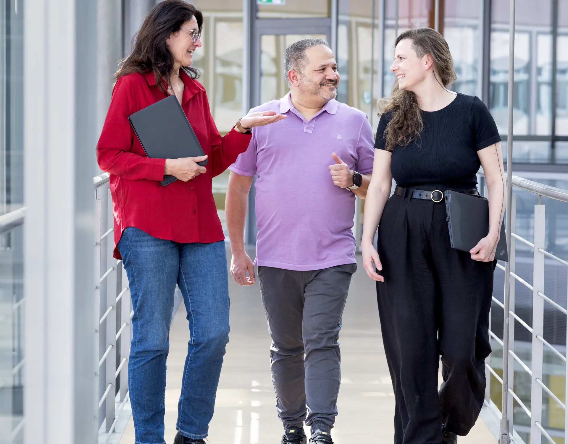 Zwei Frauen und ein Mann gehen sich unterhaltend einen Flur entlang